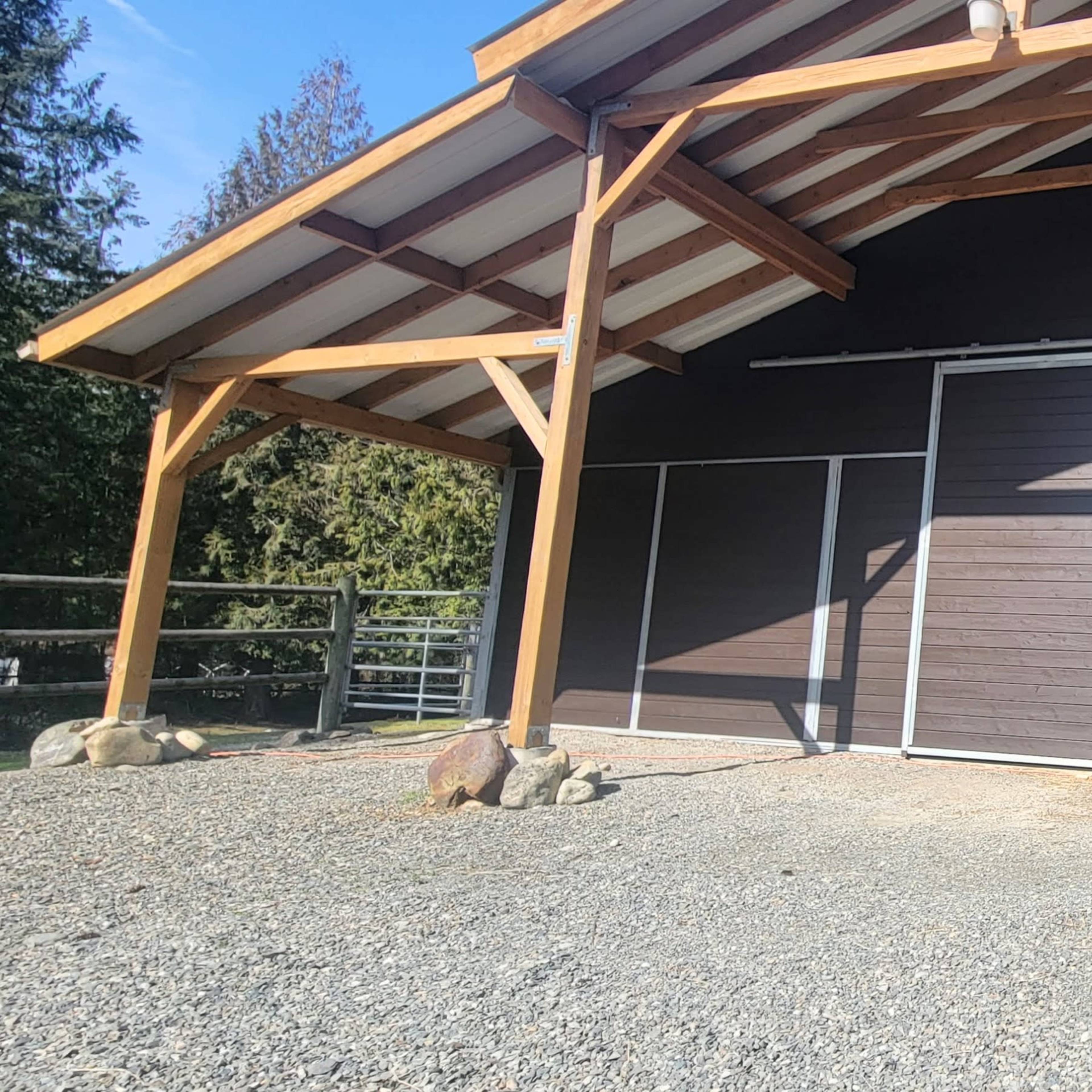 A large, dark wooden structure with a slanted roof and two sets of double doors, situated on a gravel surface.