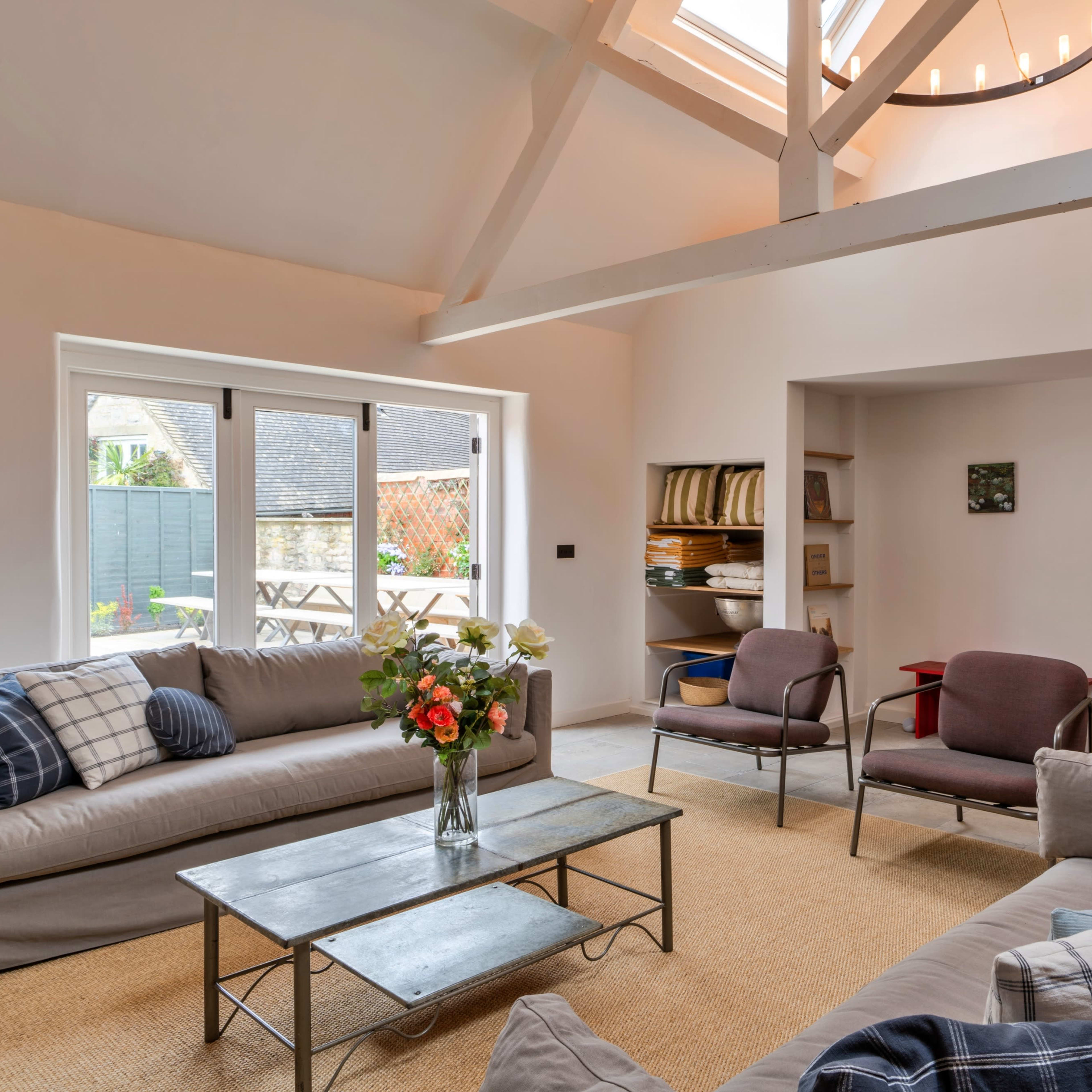 A modern living room with two sofas, a coffee table, and large windows that open to a garden area.