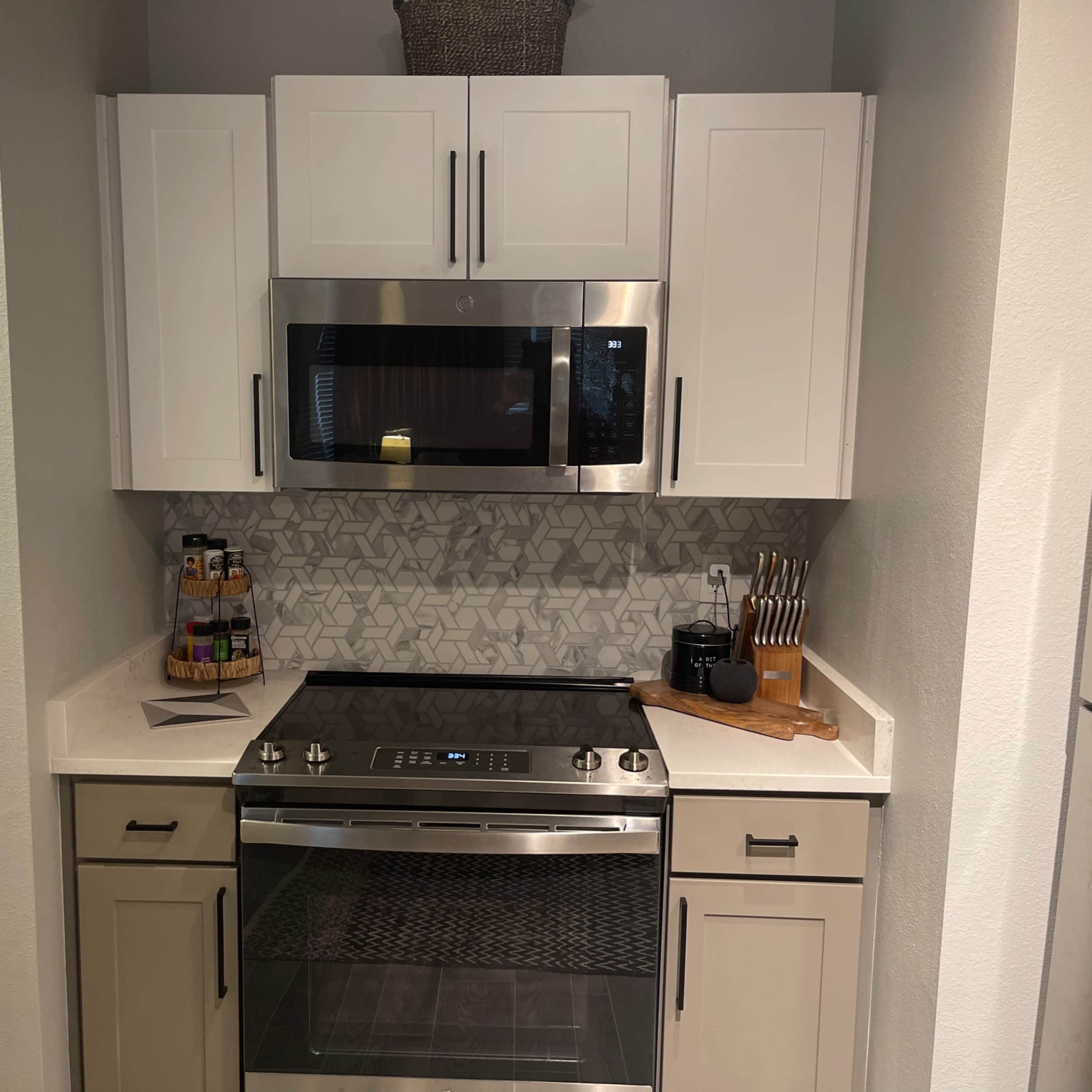 A modern kitchen with white cabinetry, a stainless steel microwave, and a black stovetop, all situated near a patterned backsplash.