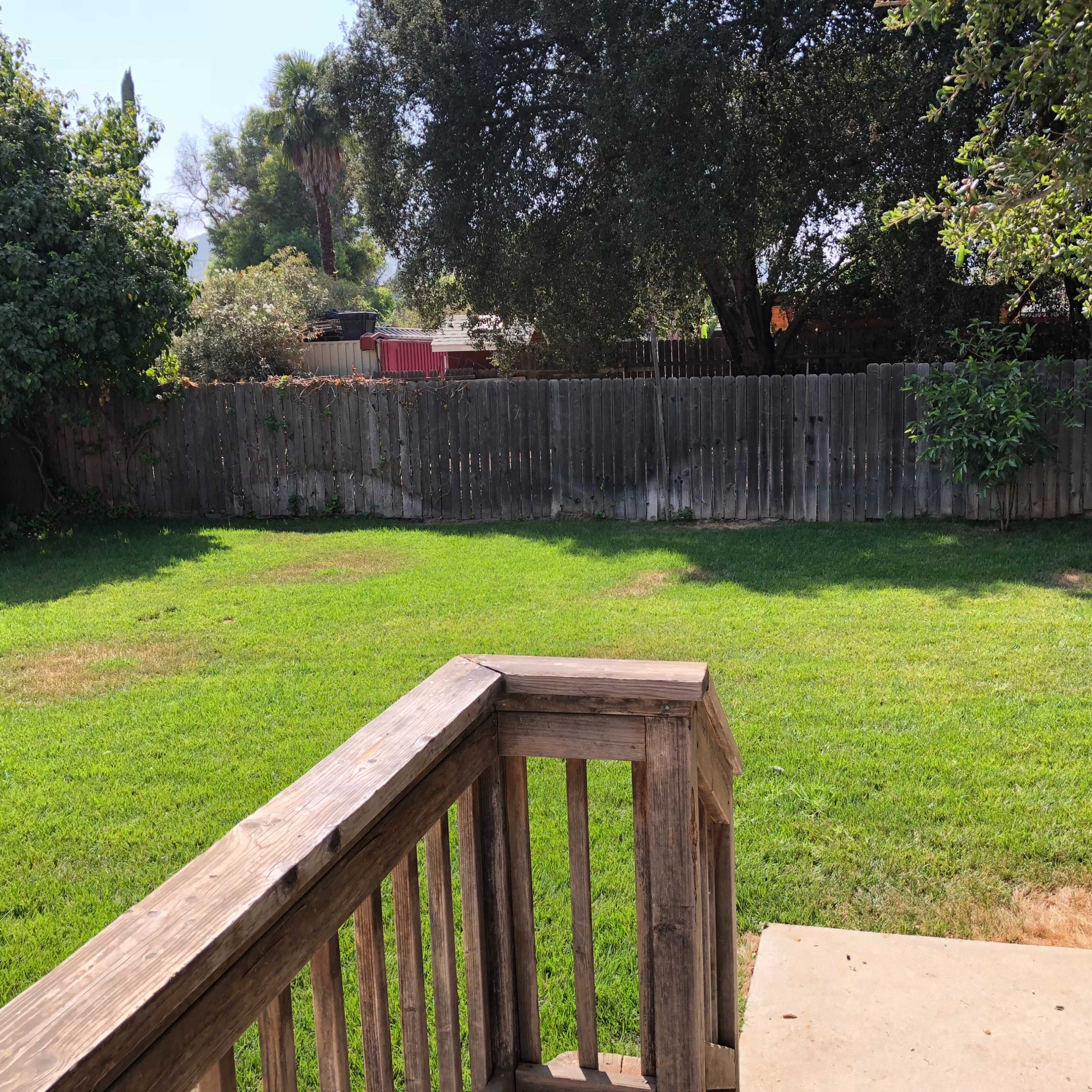 A wooden deck overlooks a grassy backyard enclosed by a wooden fence.