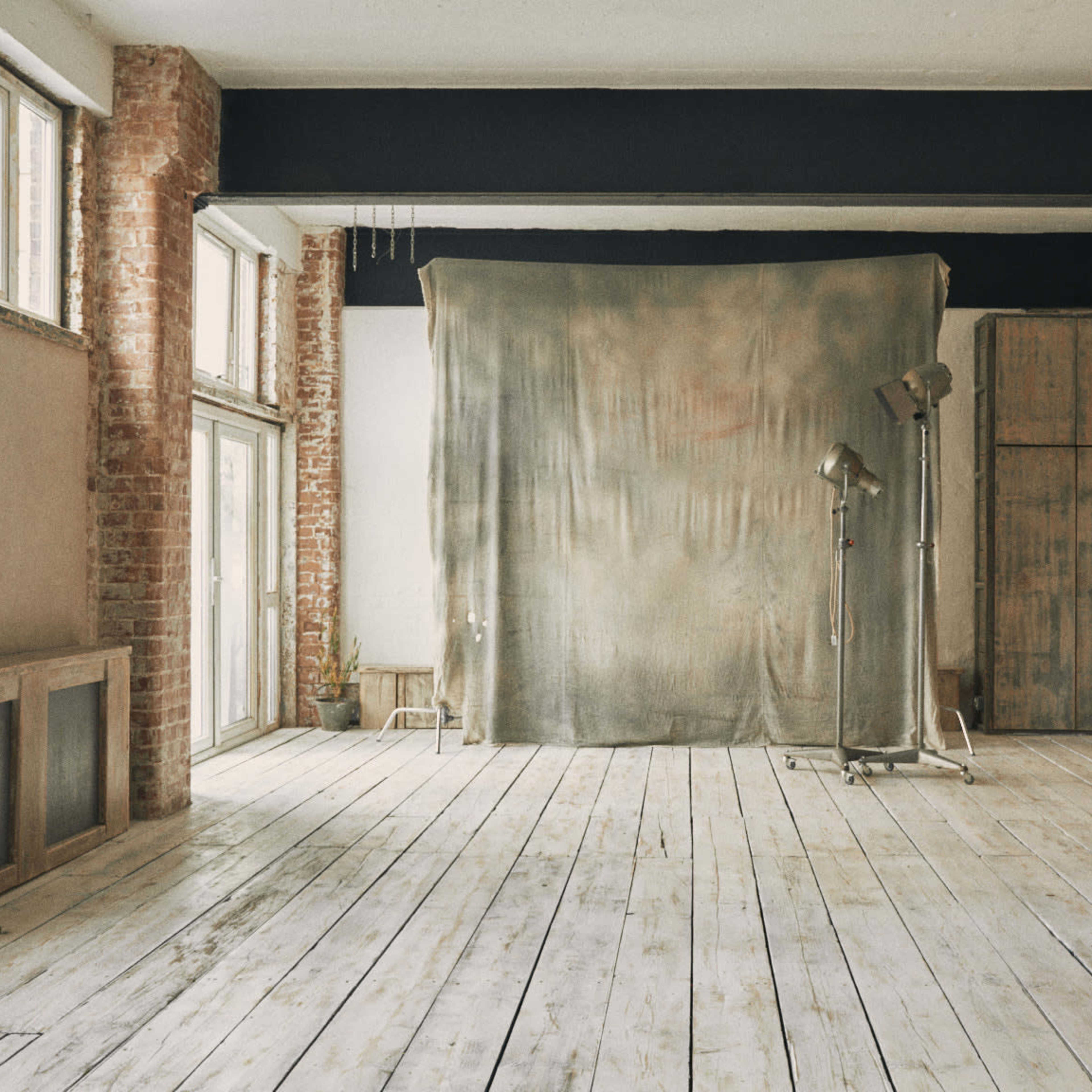 A spacious photographic studio with wooden floors, exposed brick walls, and a large fabric backdrop set up for shooting.
