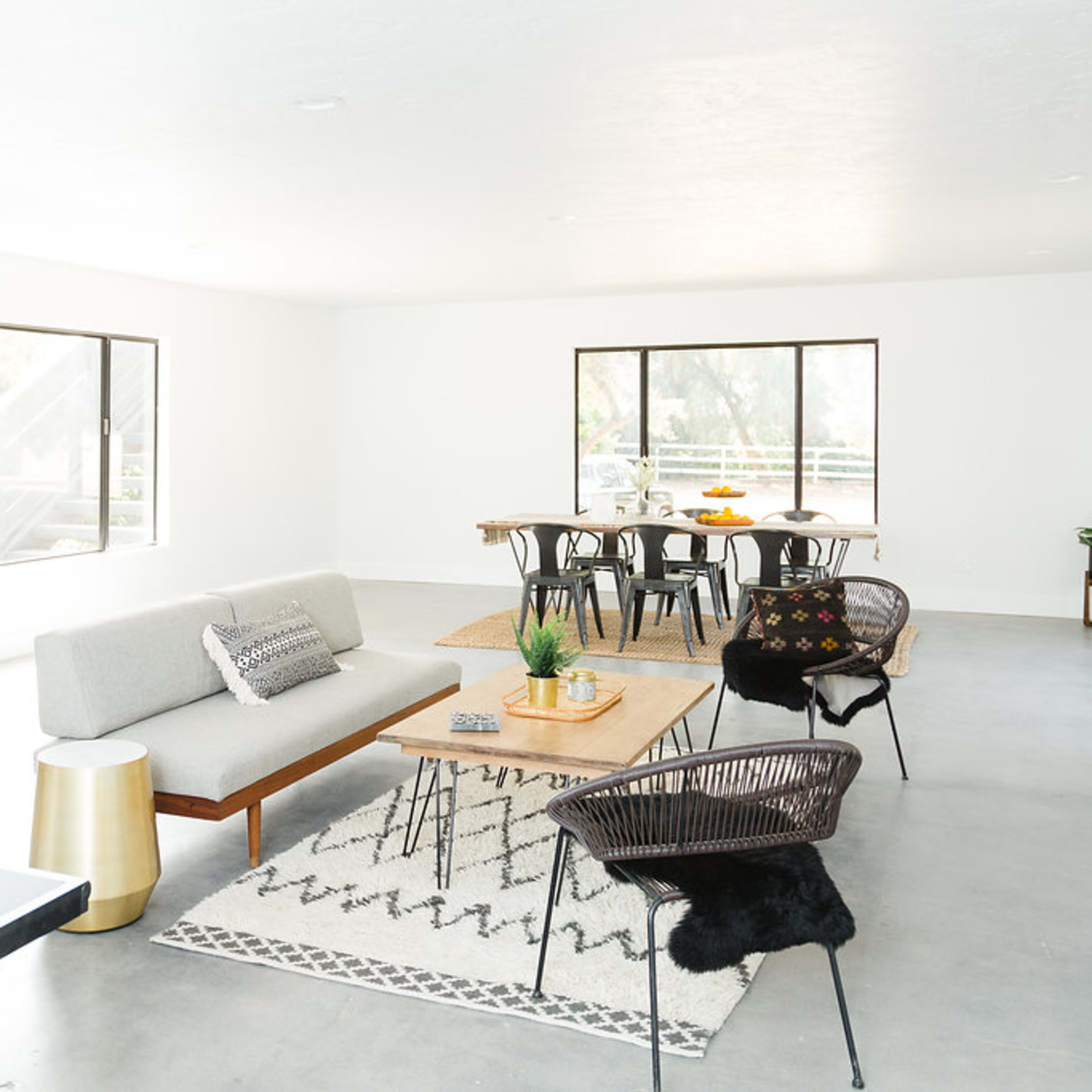 A modern, open living space with a kitchen area, a seating arrangement featuring a gray sofa and wooden coffee table, and a dining table with chairs.