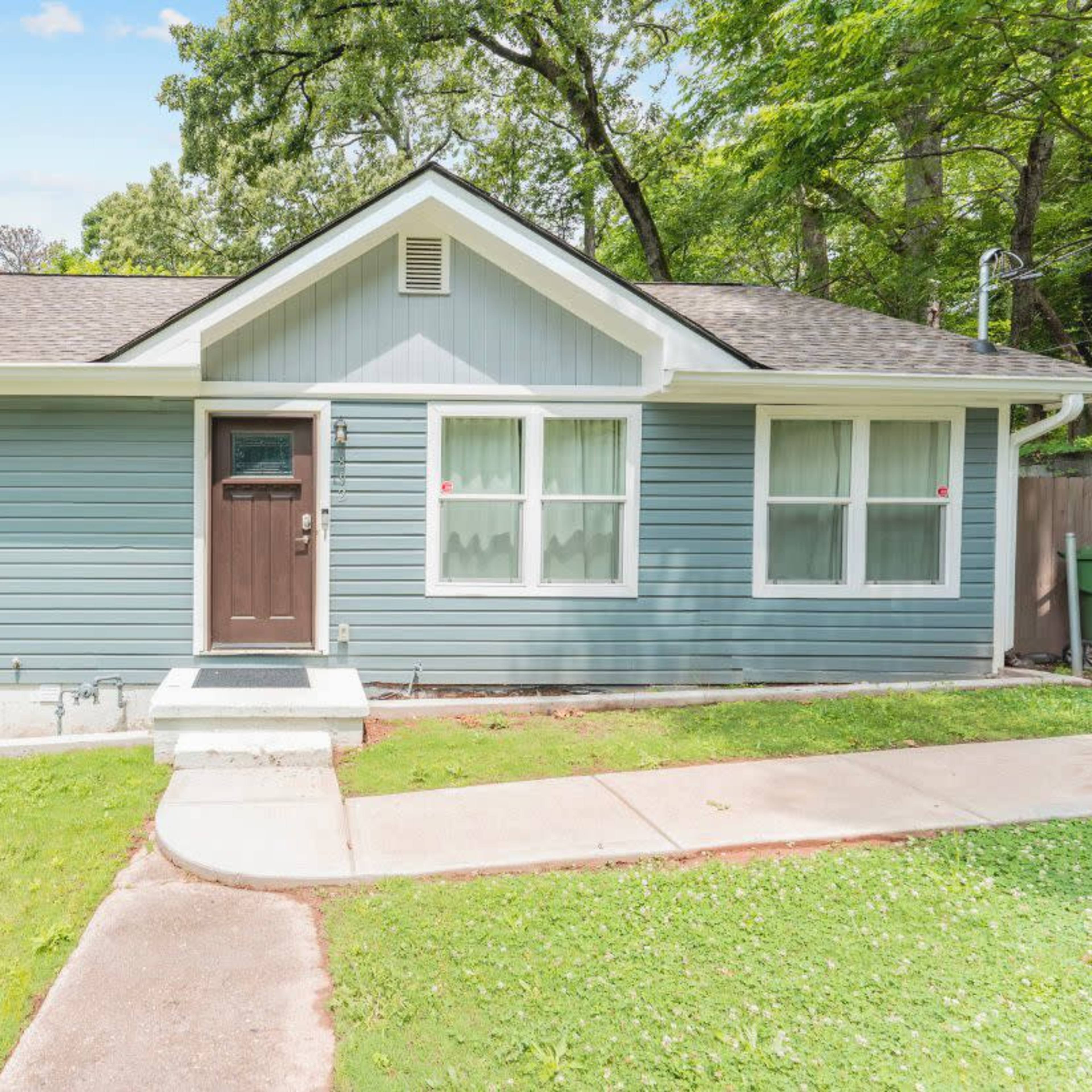 A single-story, blue-painted house with a front porch and well-maintained lawn.
