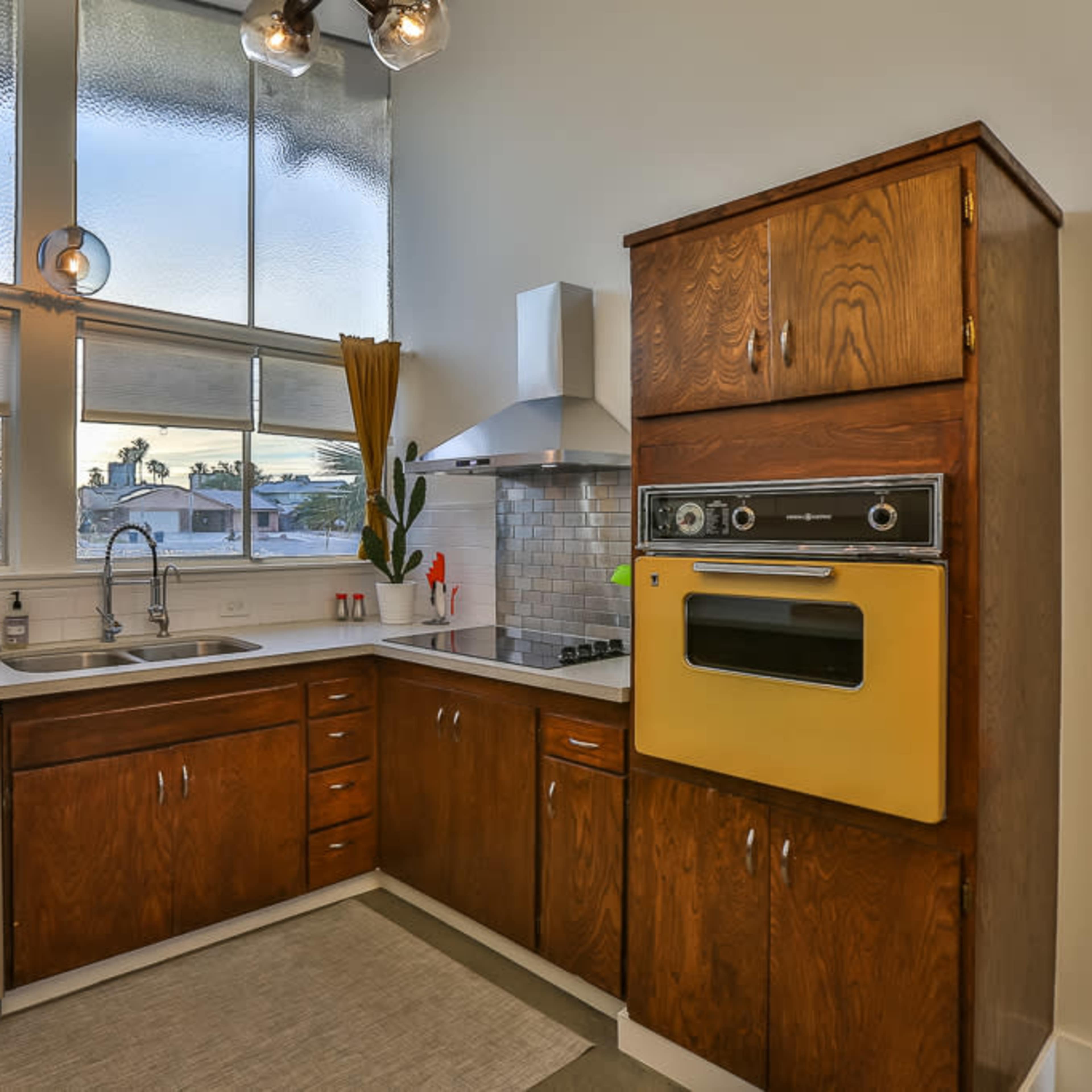 A kitchen with wooden cabinets, a yellow oven, stainless steel appliances, and large windows allowing natural light.