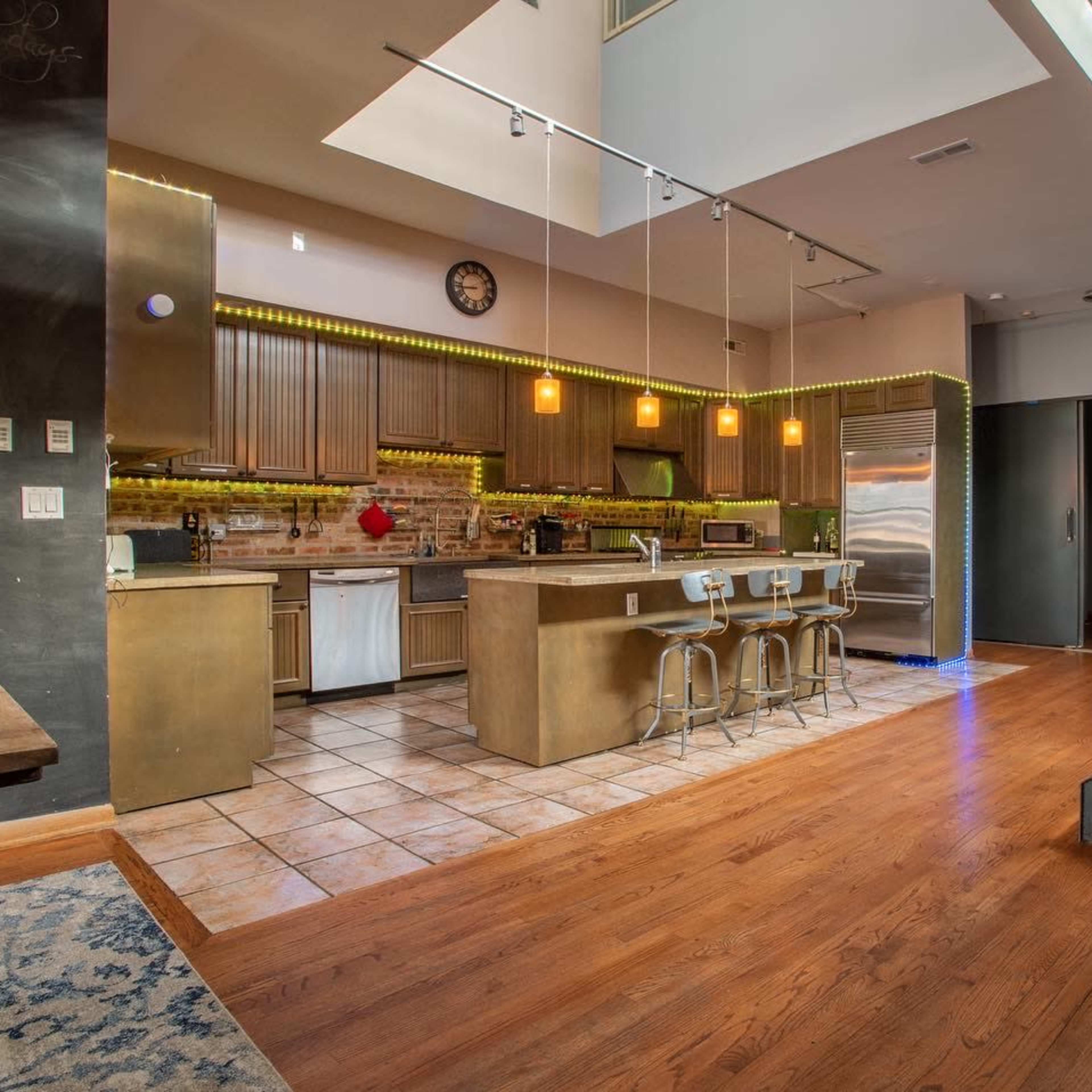 A modern kitchen with stainless steel appliances, a central island with seating, and a staircase leading to an upper level.