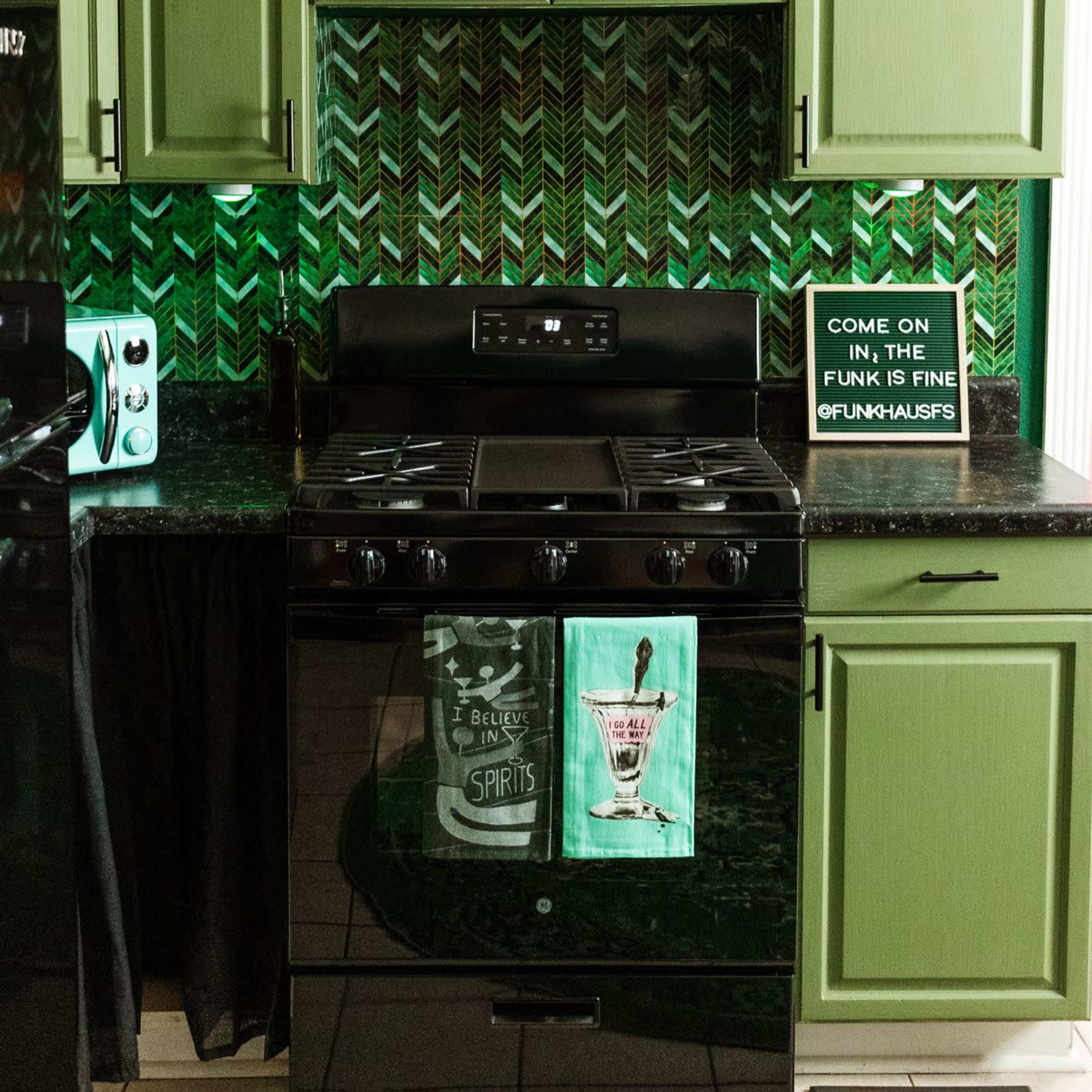 A kitchen with green cabinets, a black stove, and a patterned backsplash featuring a herringbone design.