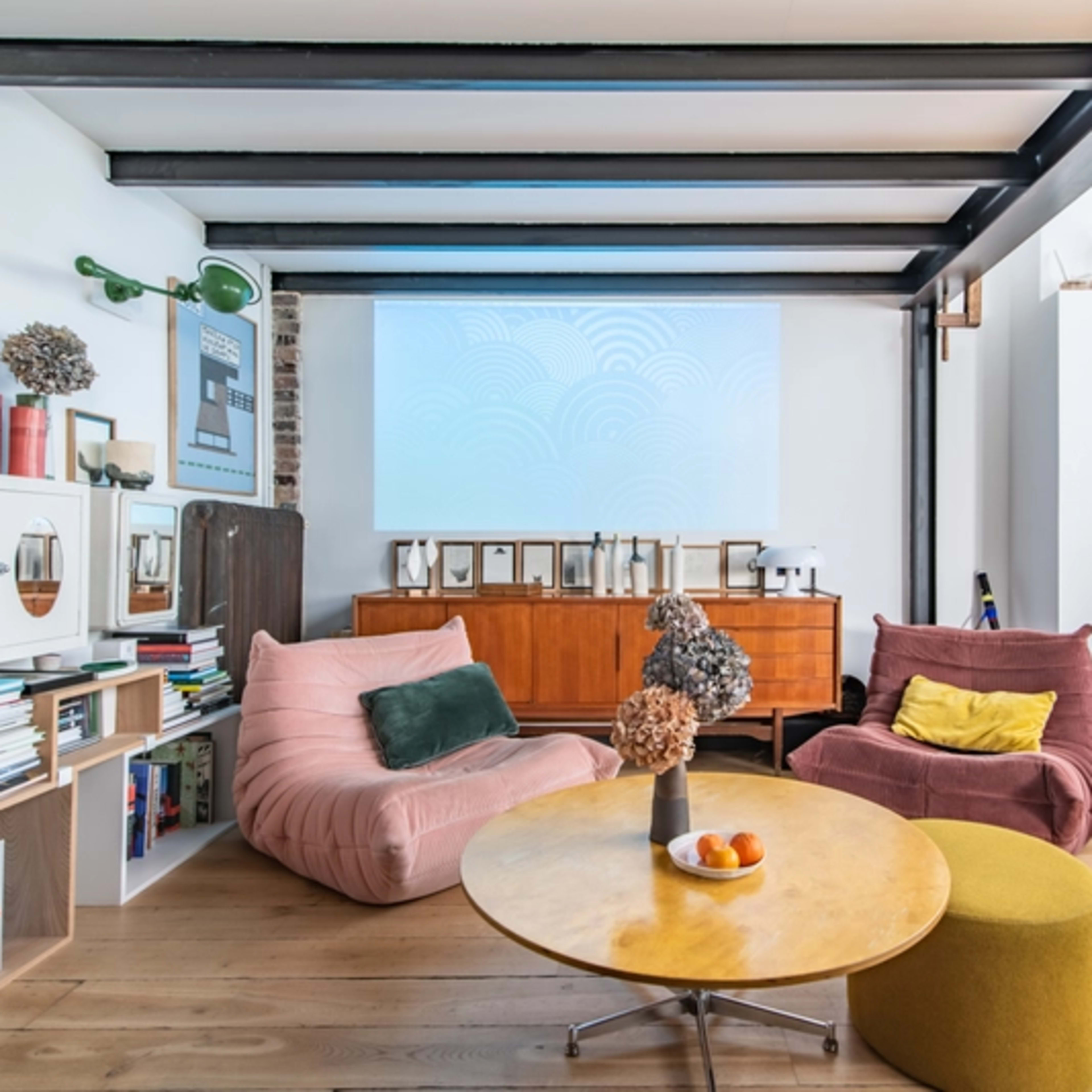 A modern living room with two bean bag chairs, a round coffee table, and a large projection screen on the wall.
