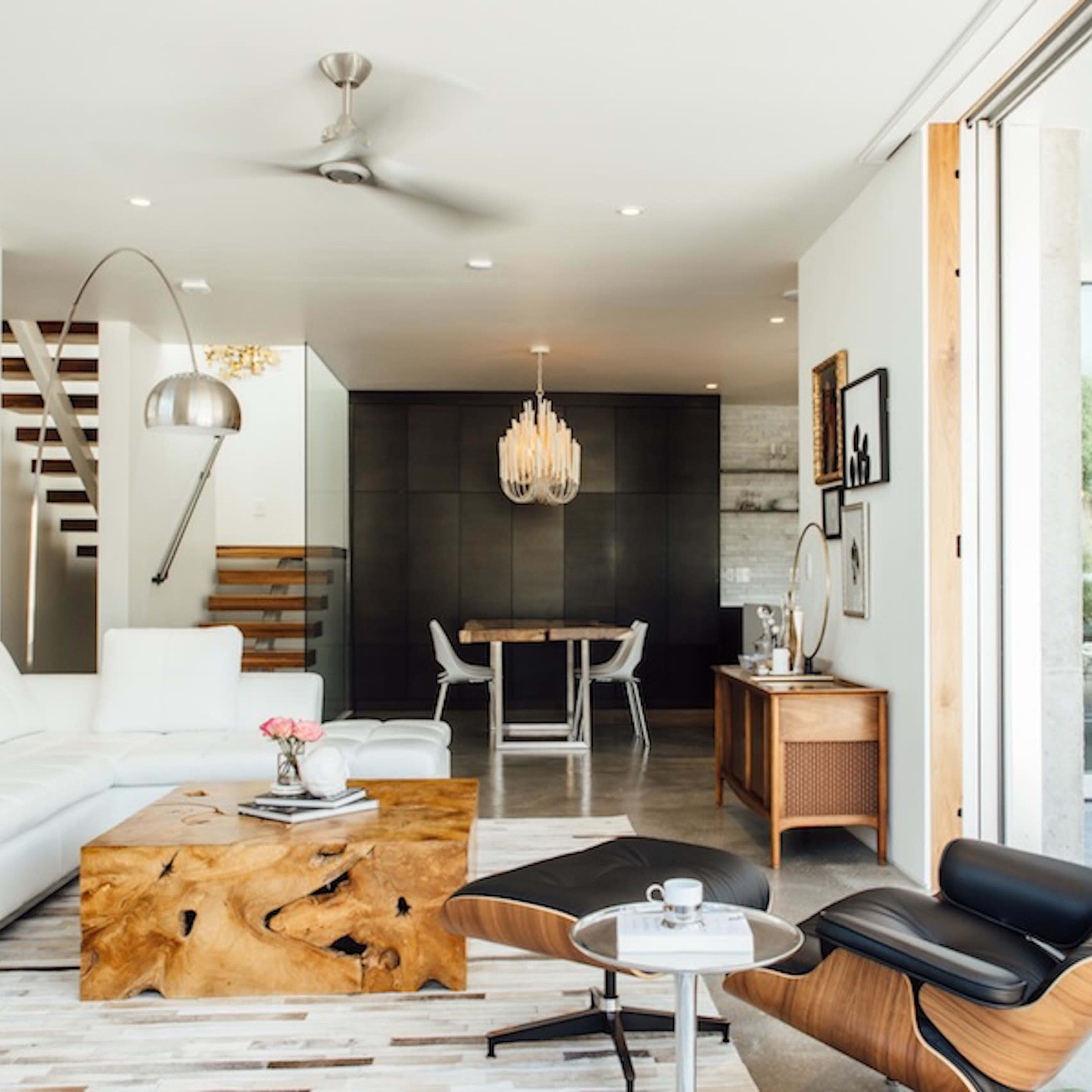 A modern living room featuring a white sectional sofa, a wooden coffee table, a sleek lounge chair, and an open layout connected to a dining area.