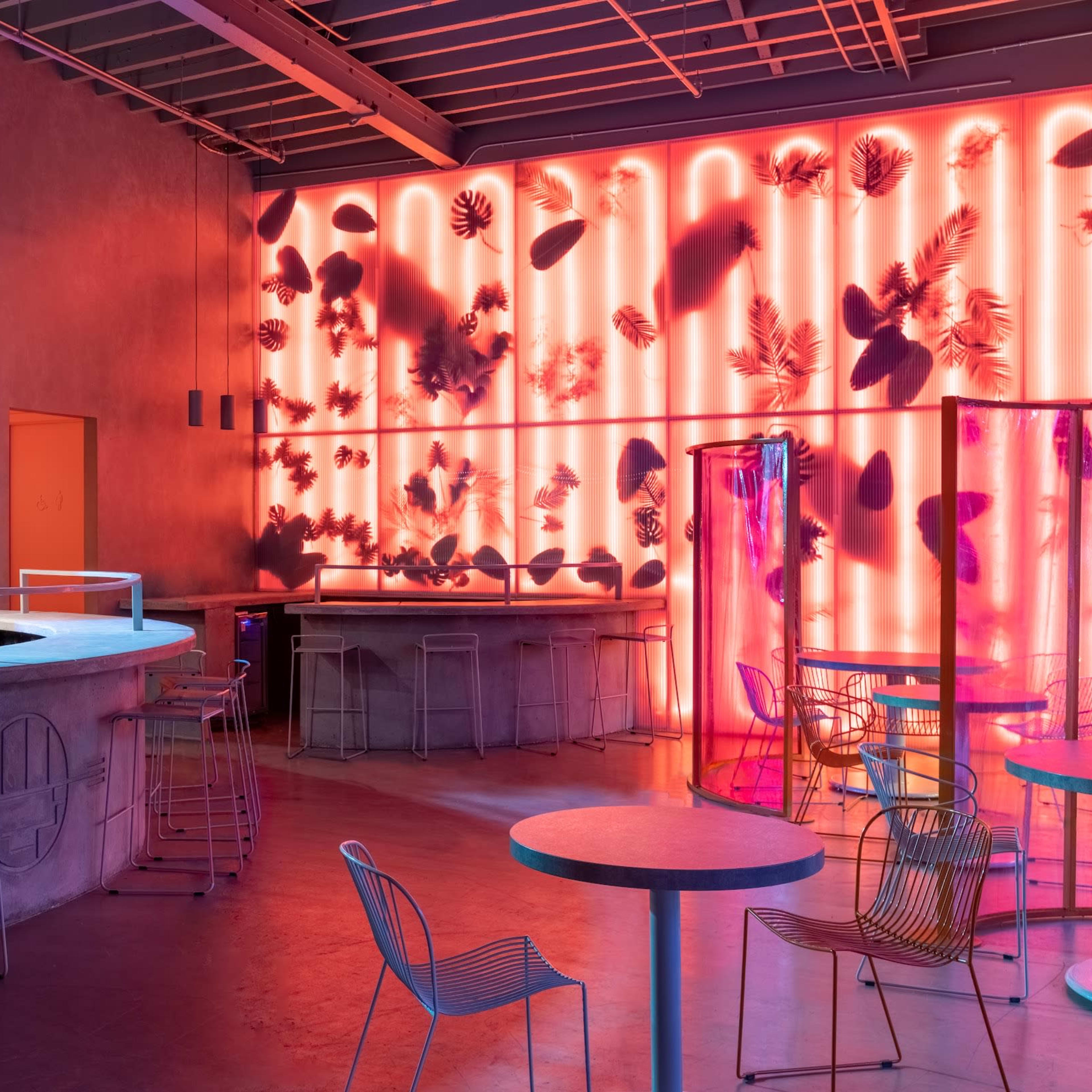 A modern bar interior with colorful lighting, circular mirrors, and a mix of seating arrangements.