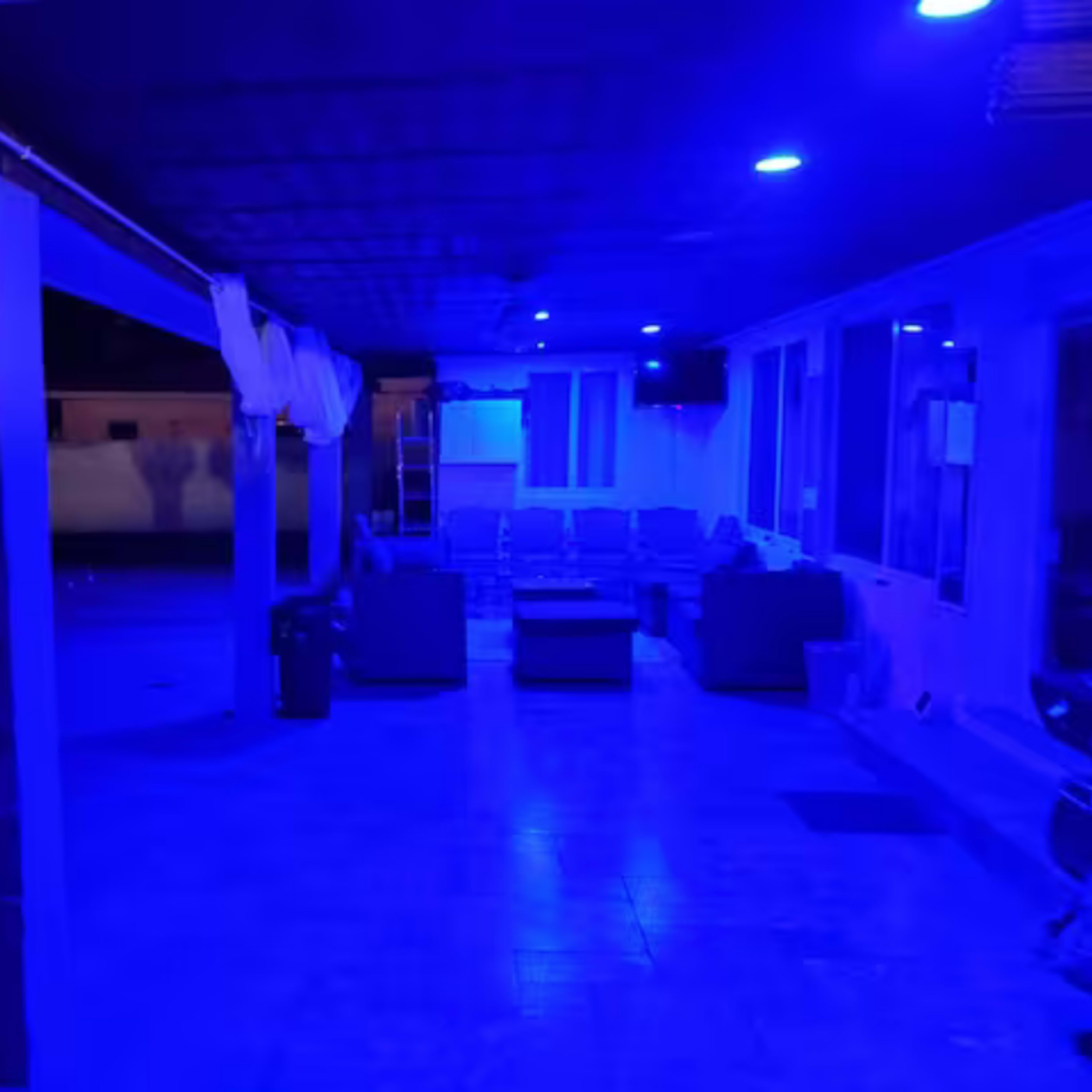 A poolside area illuminated by blue lighting, featuring lounge furniture and a covered seating space.