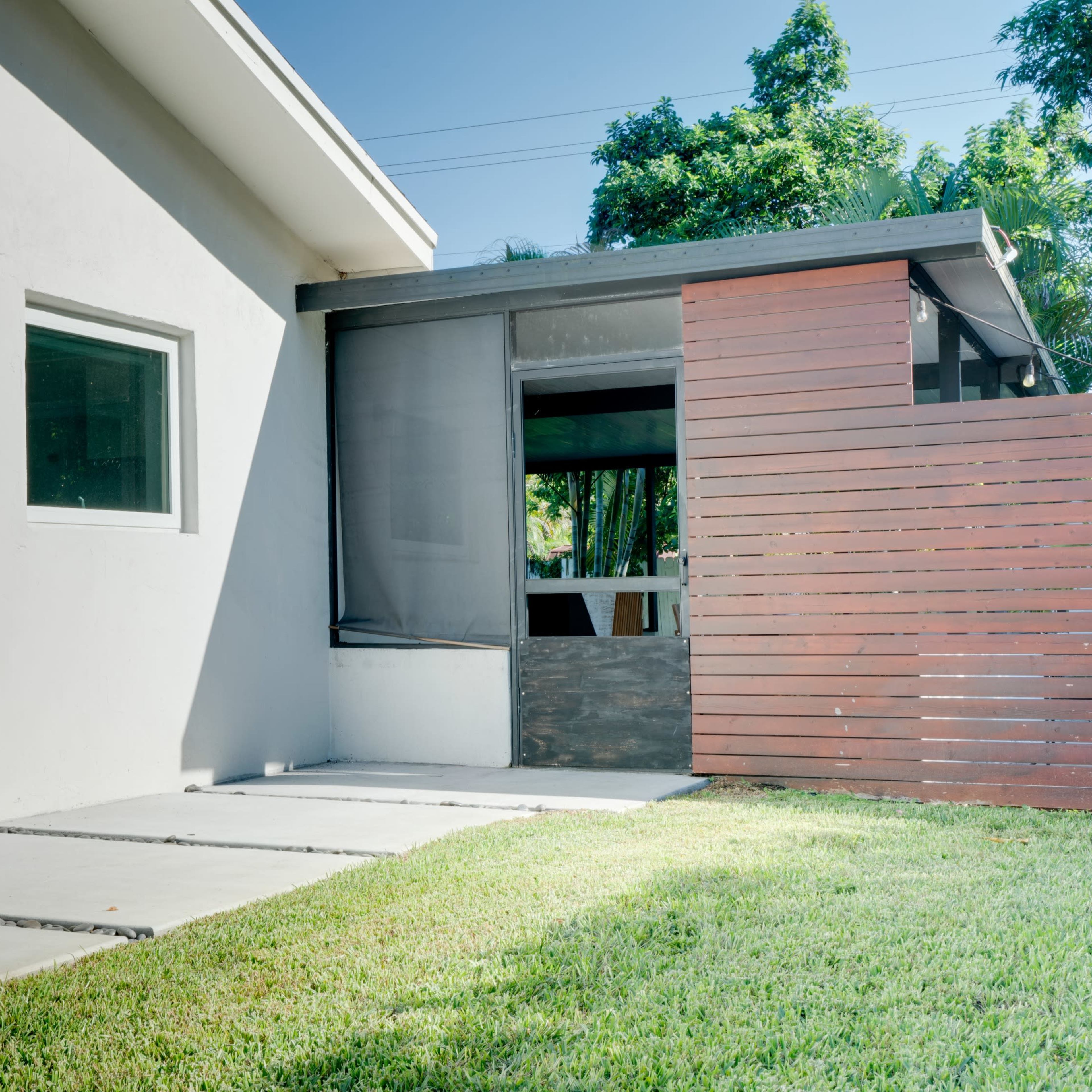 A modern house facade with a stone pathway leading to a wooden fence and an enclosed outdoor area.