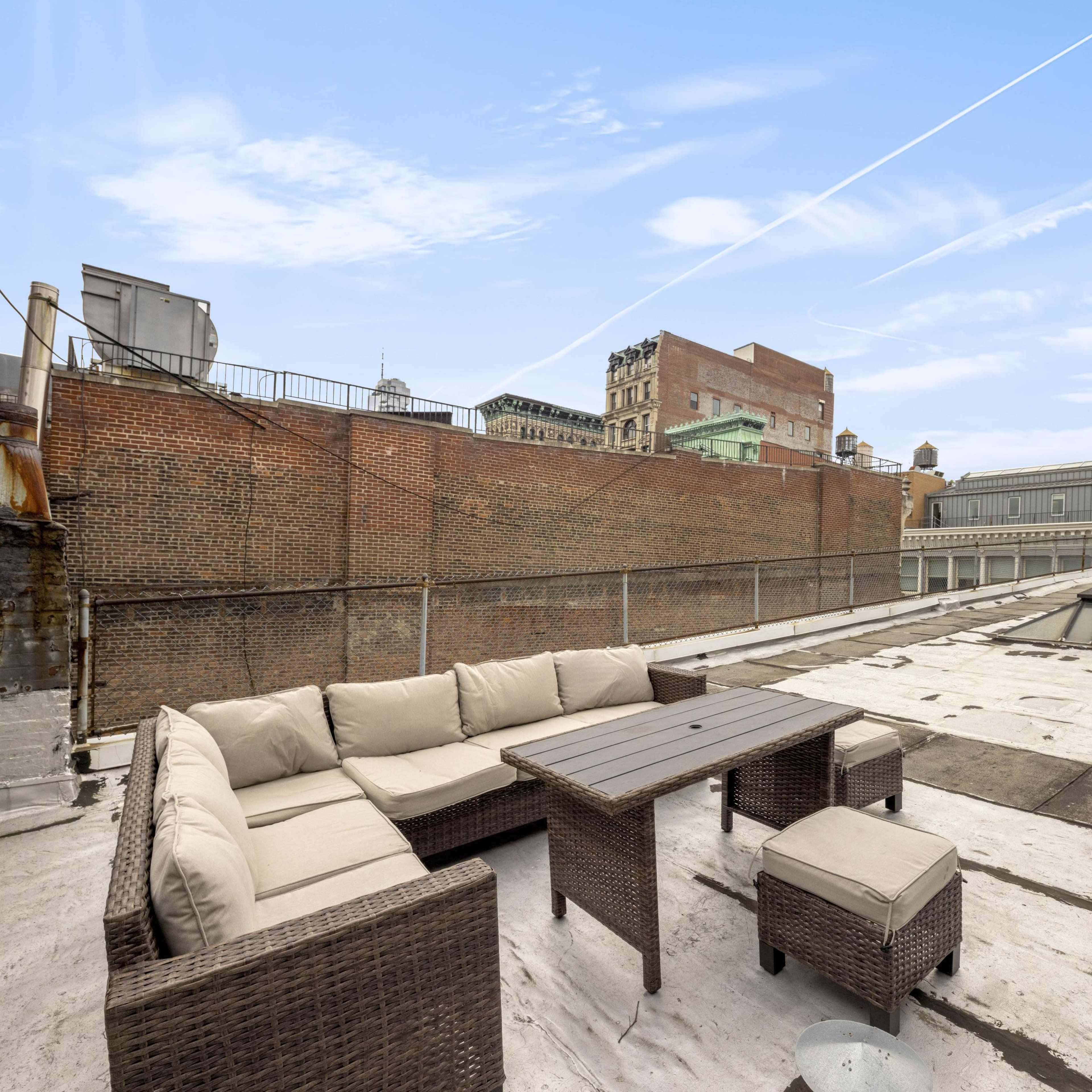 A rooftop terrace featuring a sectional sofa and a table overlooking urban buildings.