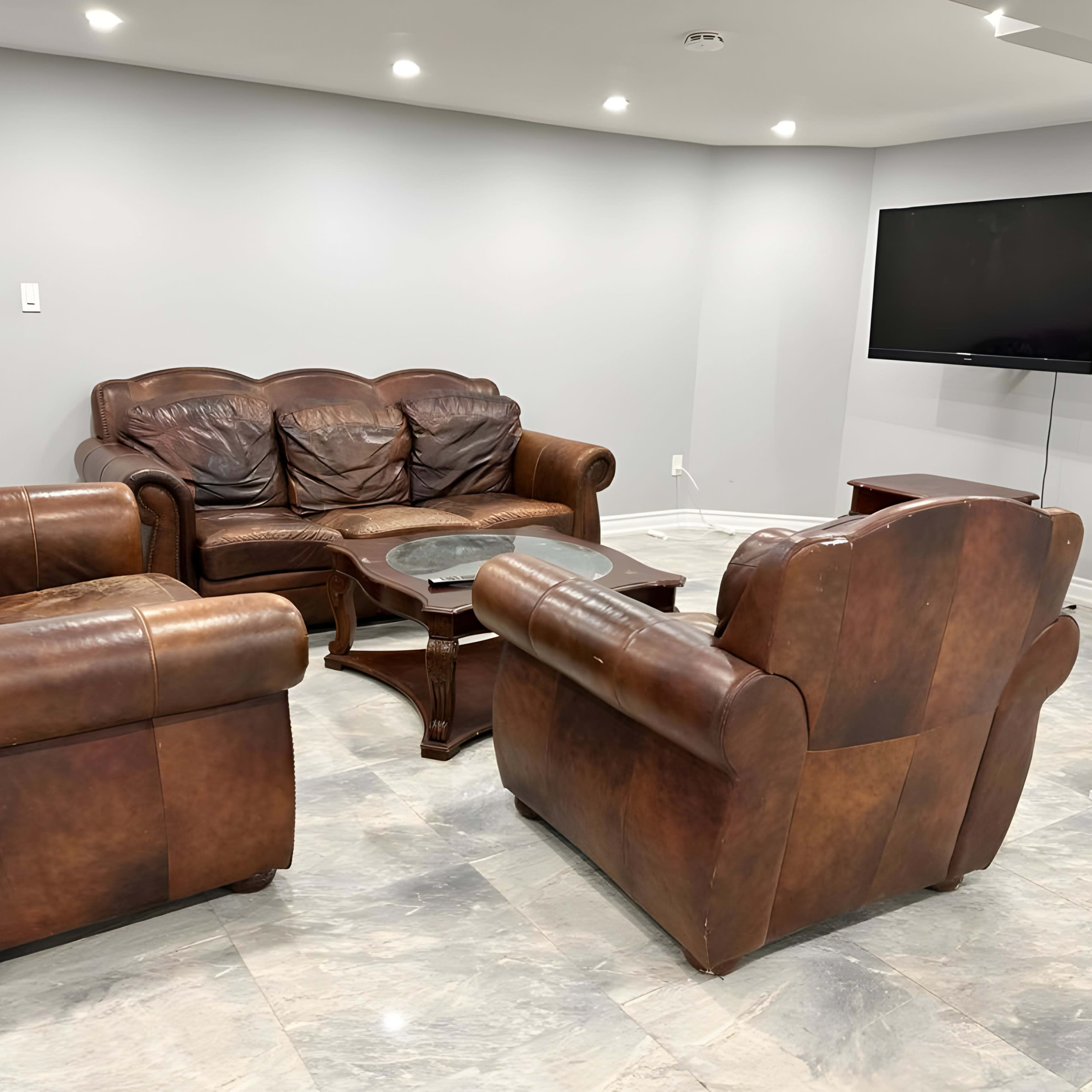 A living room with brown leather couches, a wooden coffee table, and a wall-mounted television in a light grey setting.