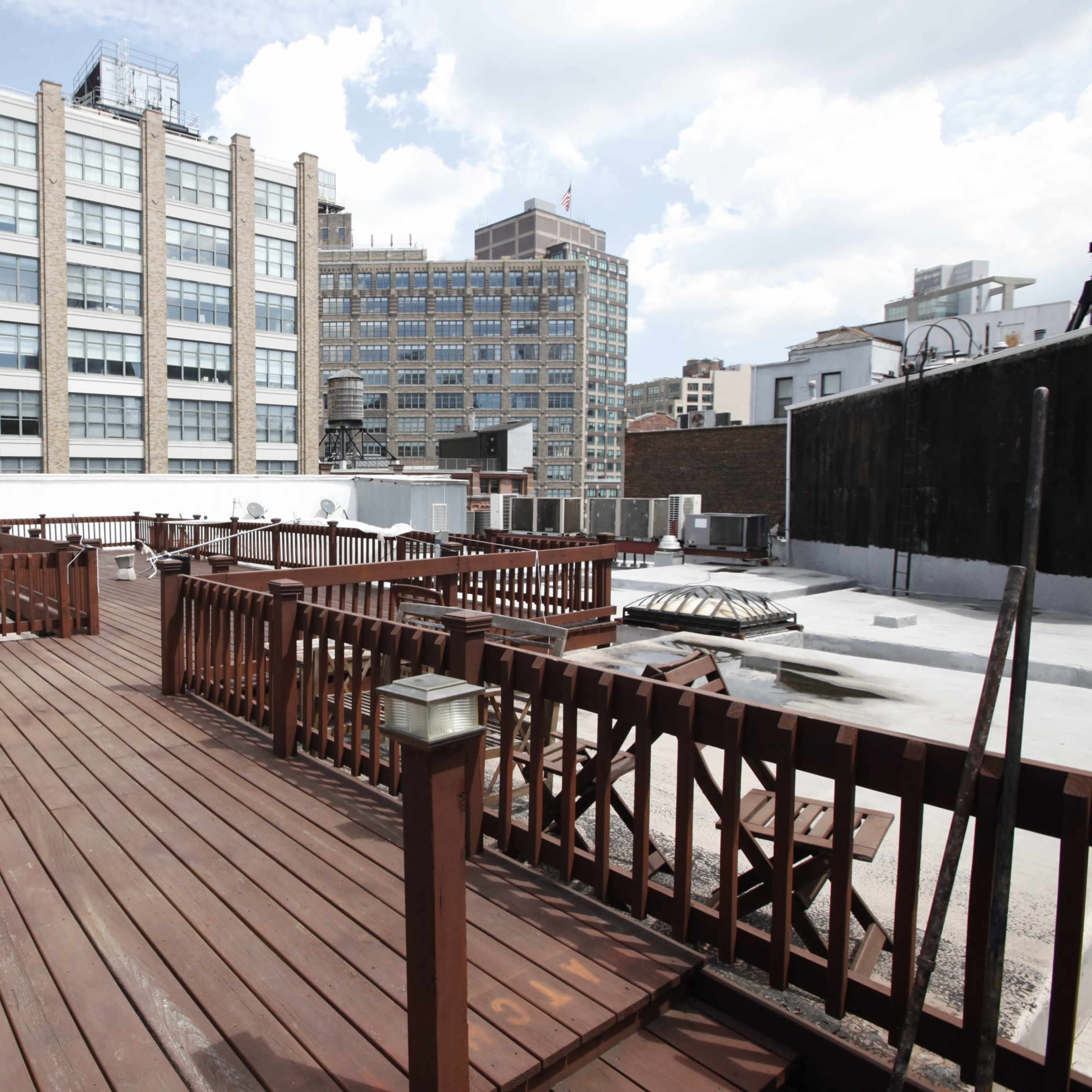 A wooden deck on a rooftop, surrounded by various buildings under a partly cloudy sky.