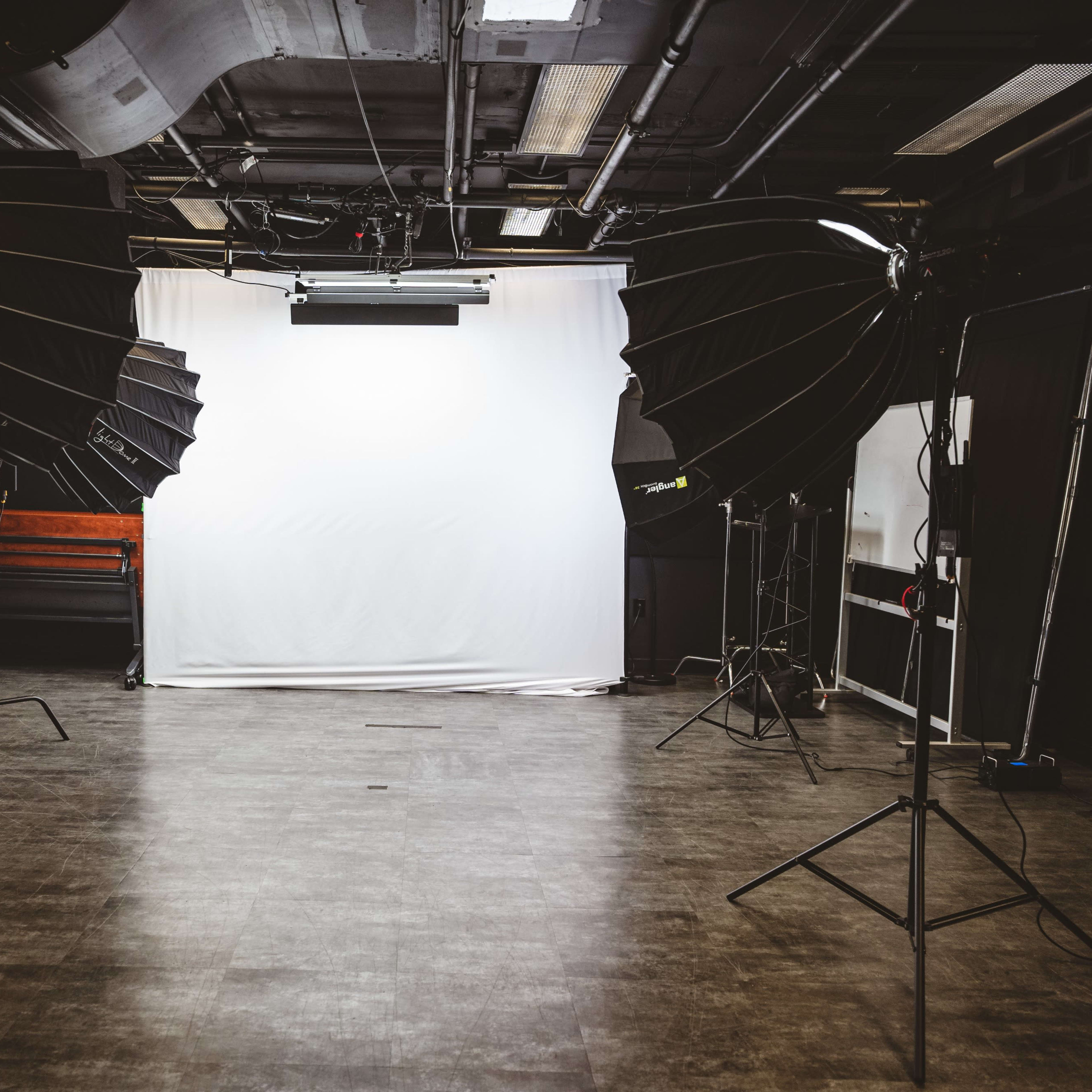 A photography studio features two large softbox lights positioned on either side of a white backdrop.