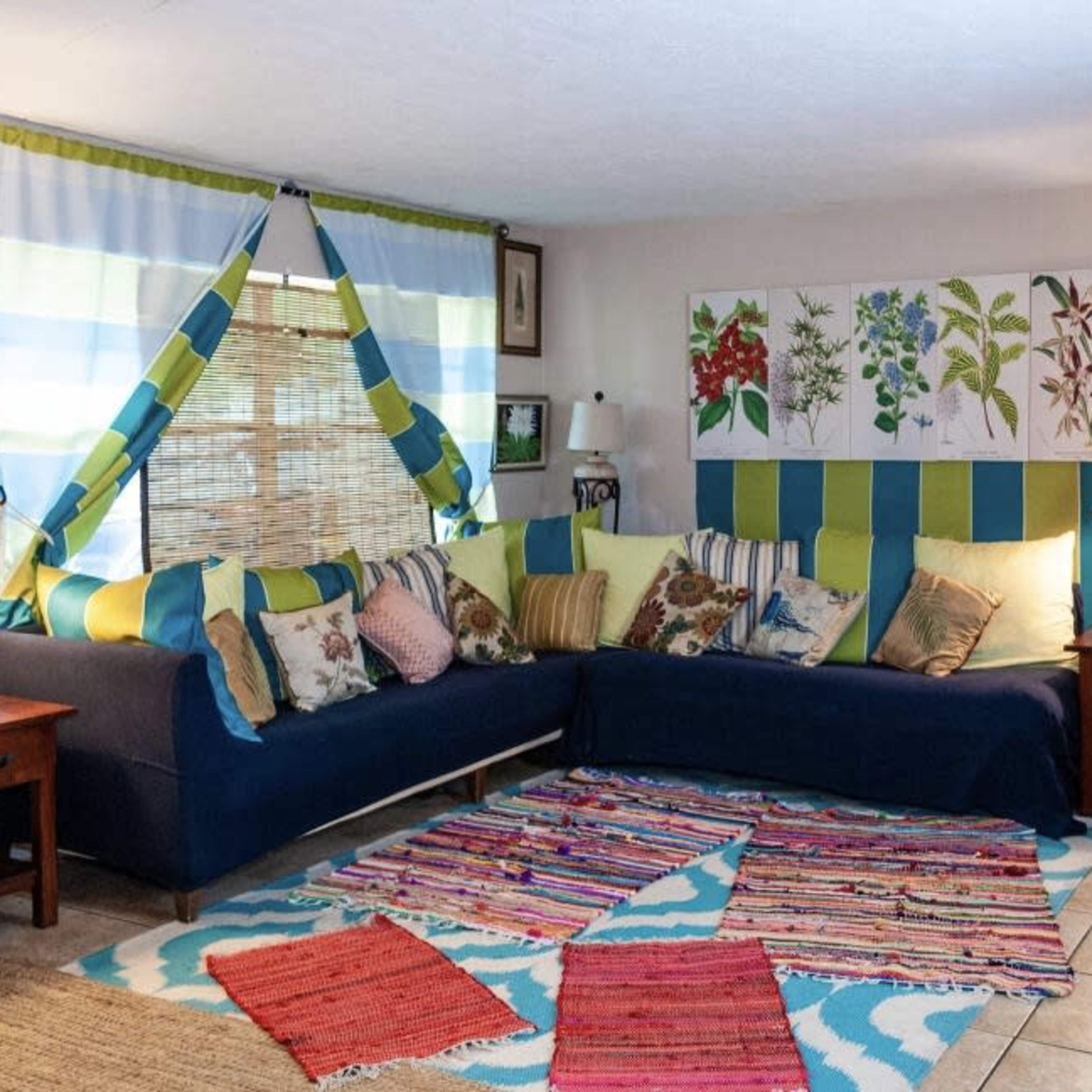 A living room features a sectional couch with colorful cushions, a patterned rug, and two lamps on wooden side tables.
