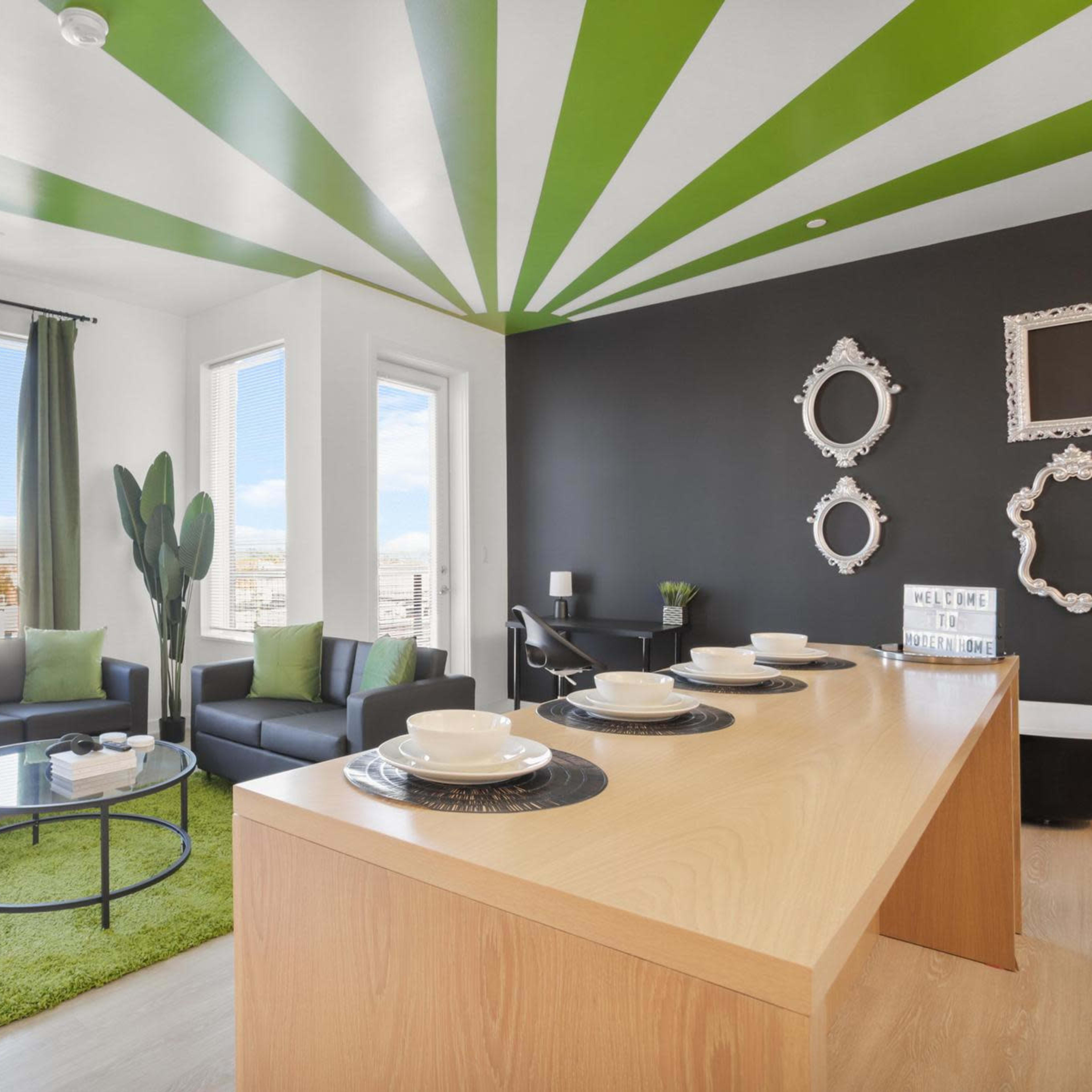 A modern living room with a striped green and white ceiling, a black accent wall, potted plants, and a wooden dining table set with plates.