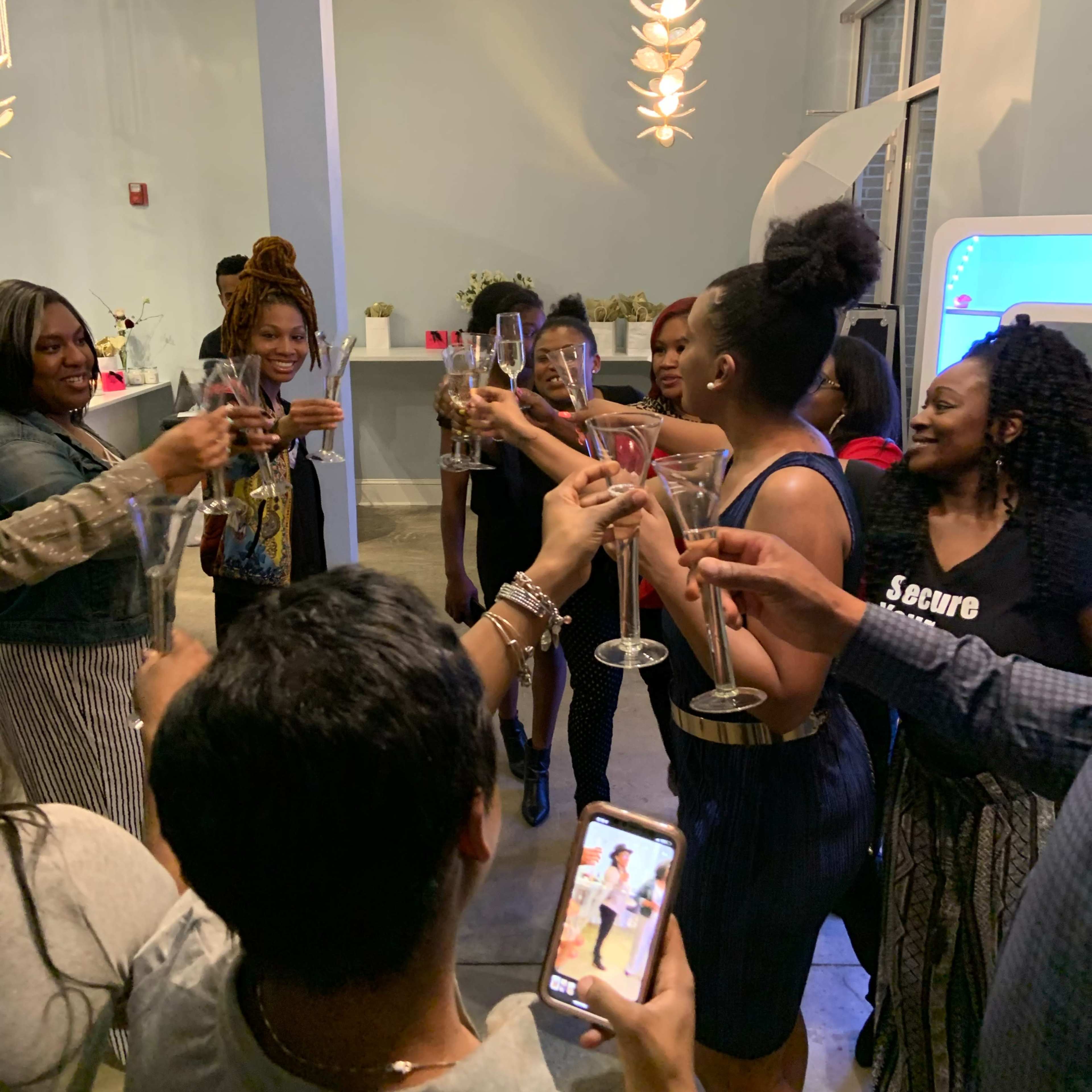A group of people stands together, holding up glasses in a toast while smiling and celebrating indoors.