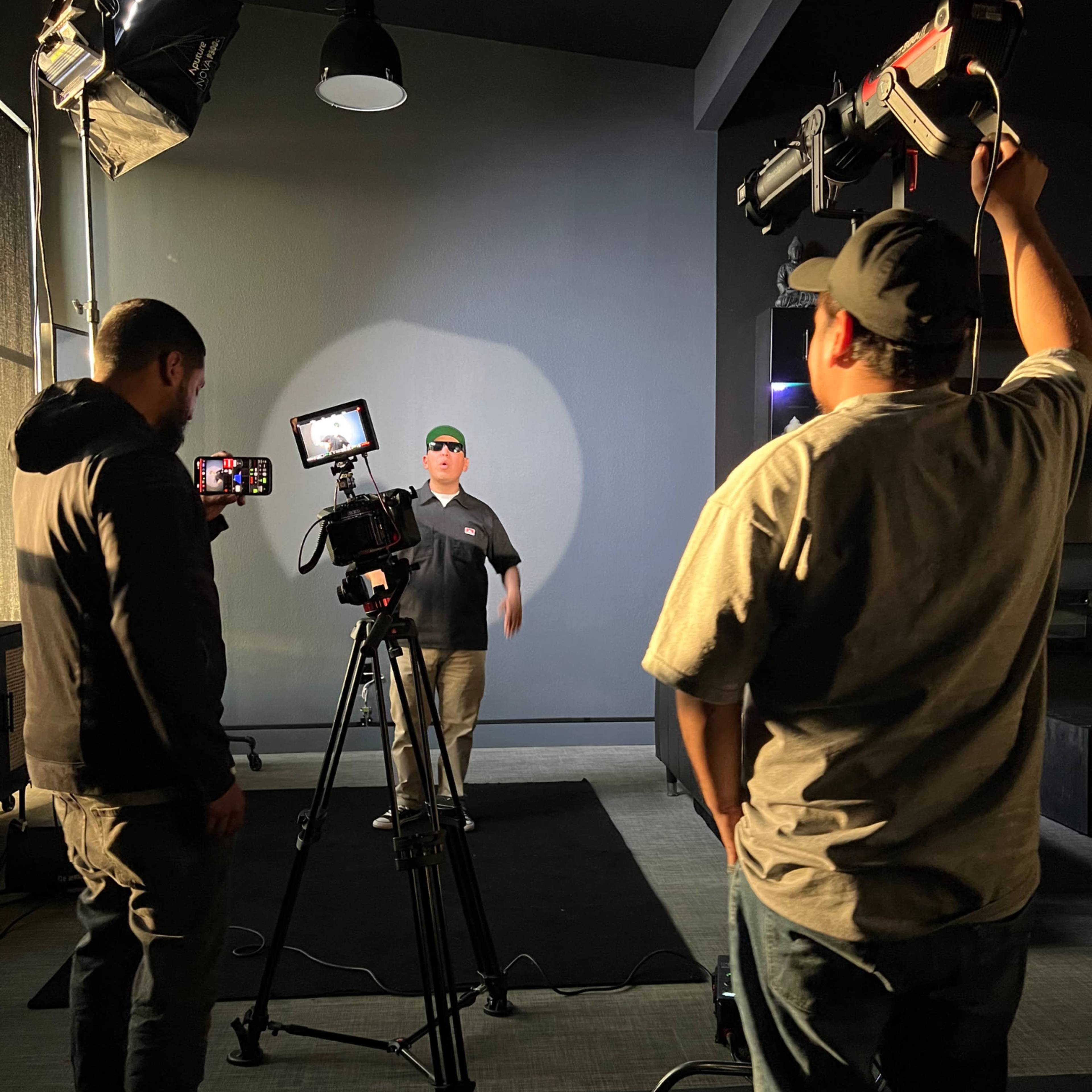 Three people are filming a scene with a camera setup and lighting equipment in a studio setting.