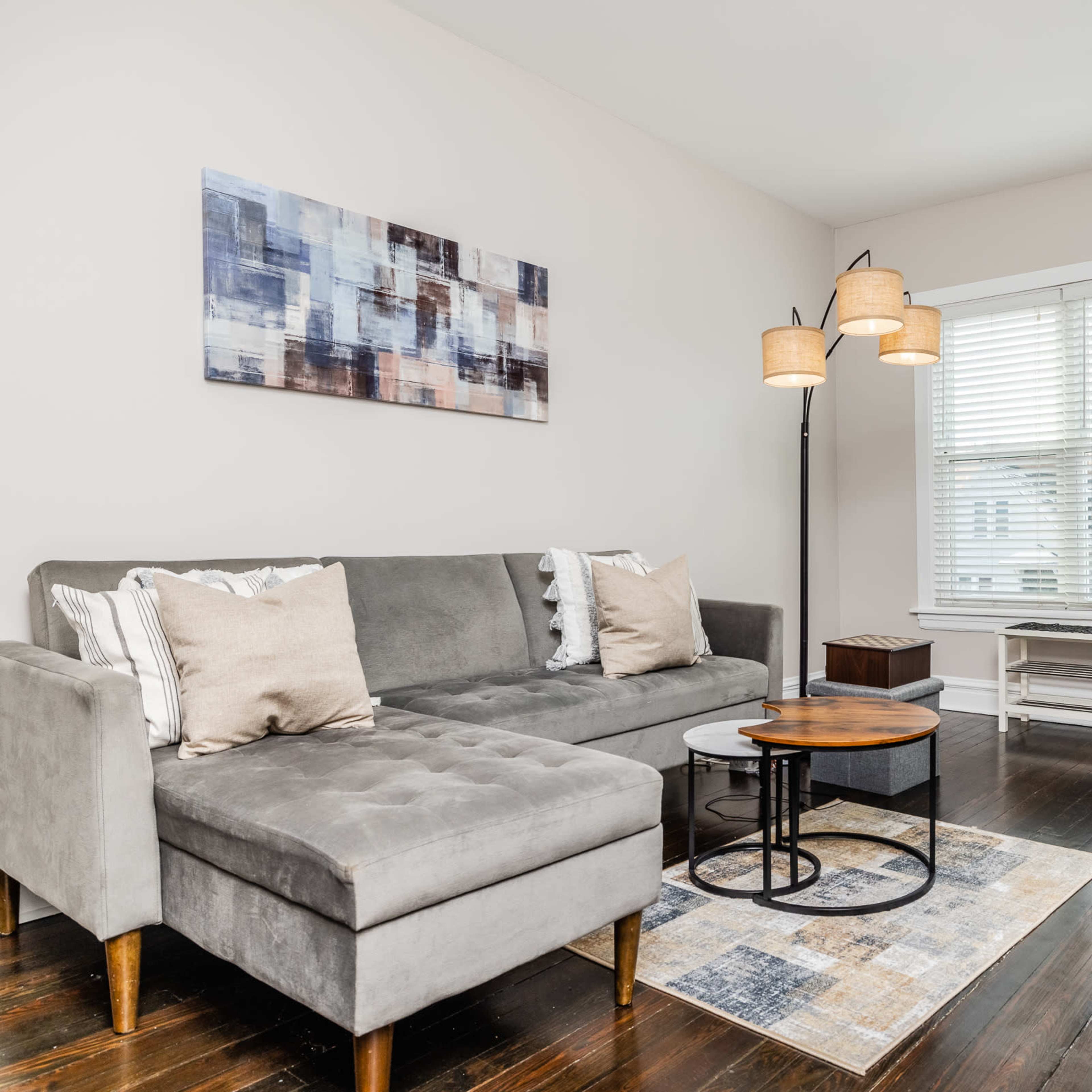 A modern living room featuring a gray sectional sofa, a circular coffee table, and a large window with blinds.