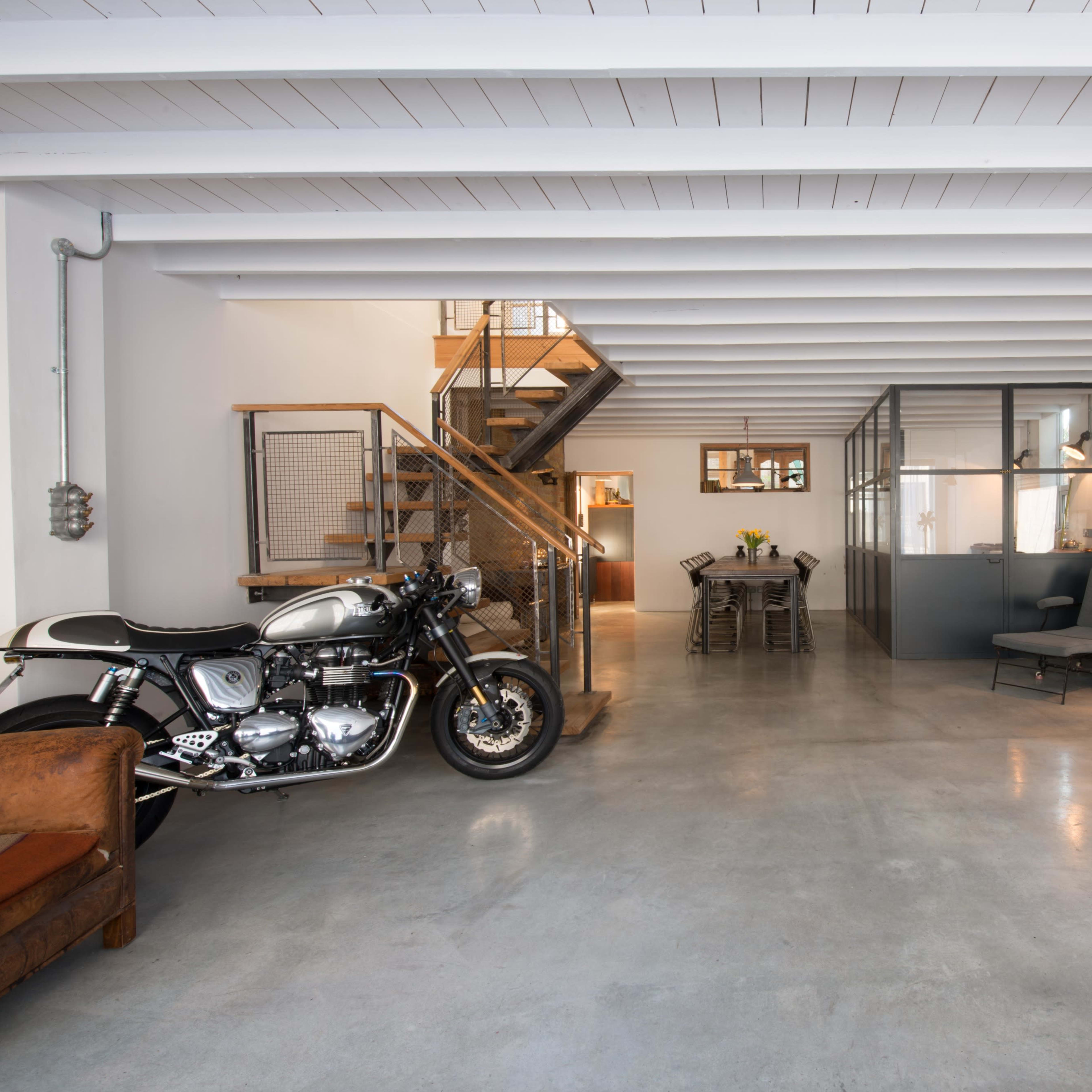 A spacious interior featuring a motorcycle, a wooden staircase, a dining table, and a seating area with vintage furniture.