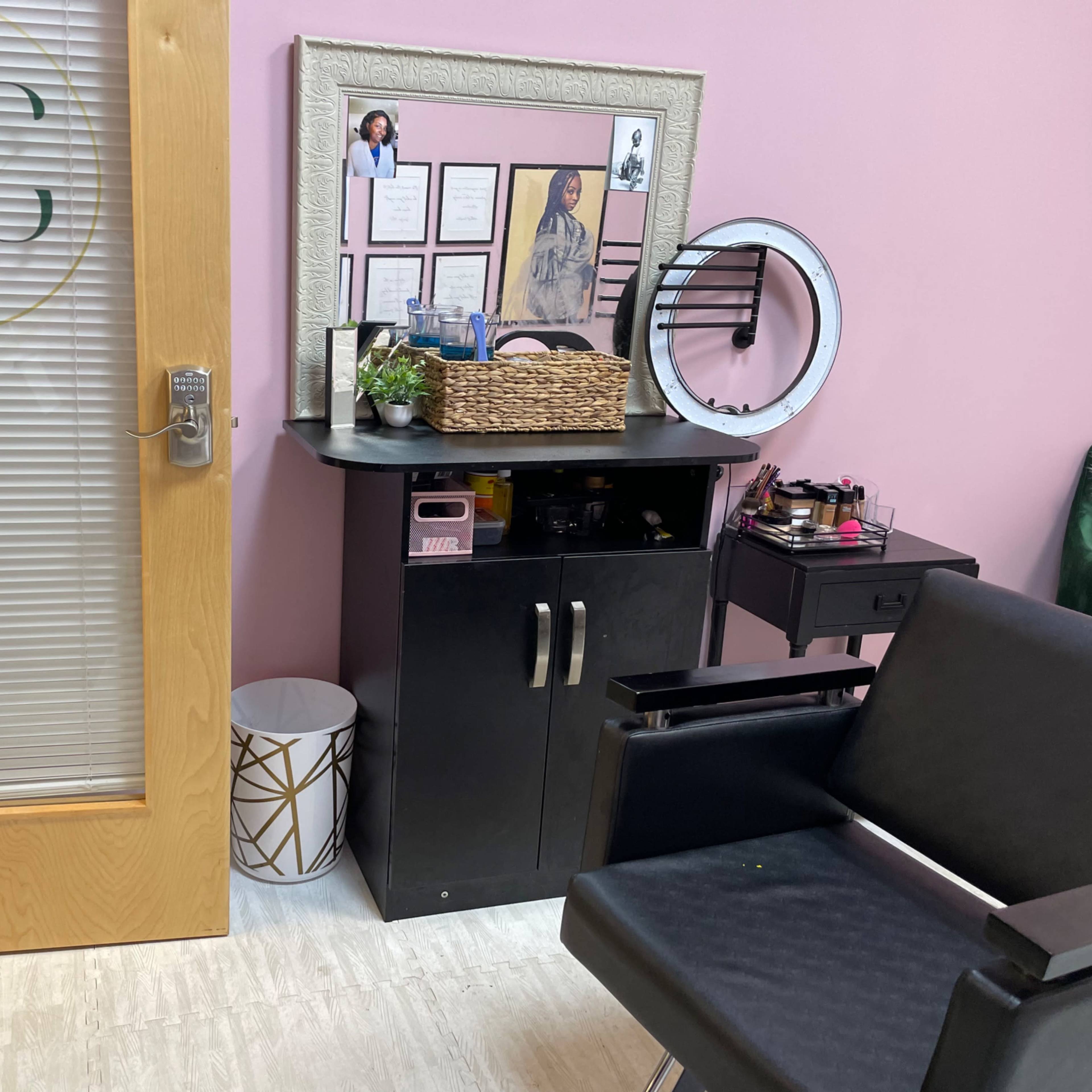 A beauty treatment room featuring a wooden door with the initials "KS," a black vanity with various beauty products, and a comfortable chair next to a patterned wastebasket.