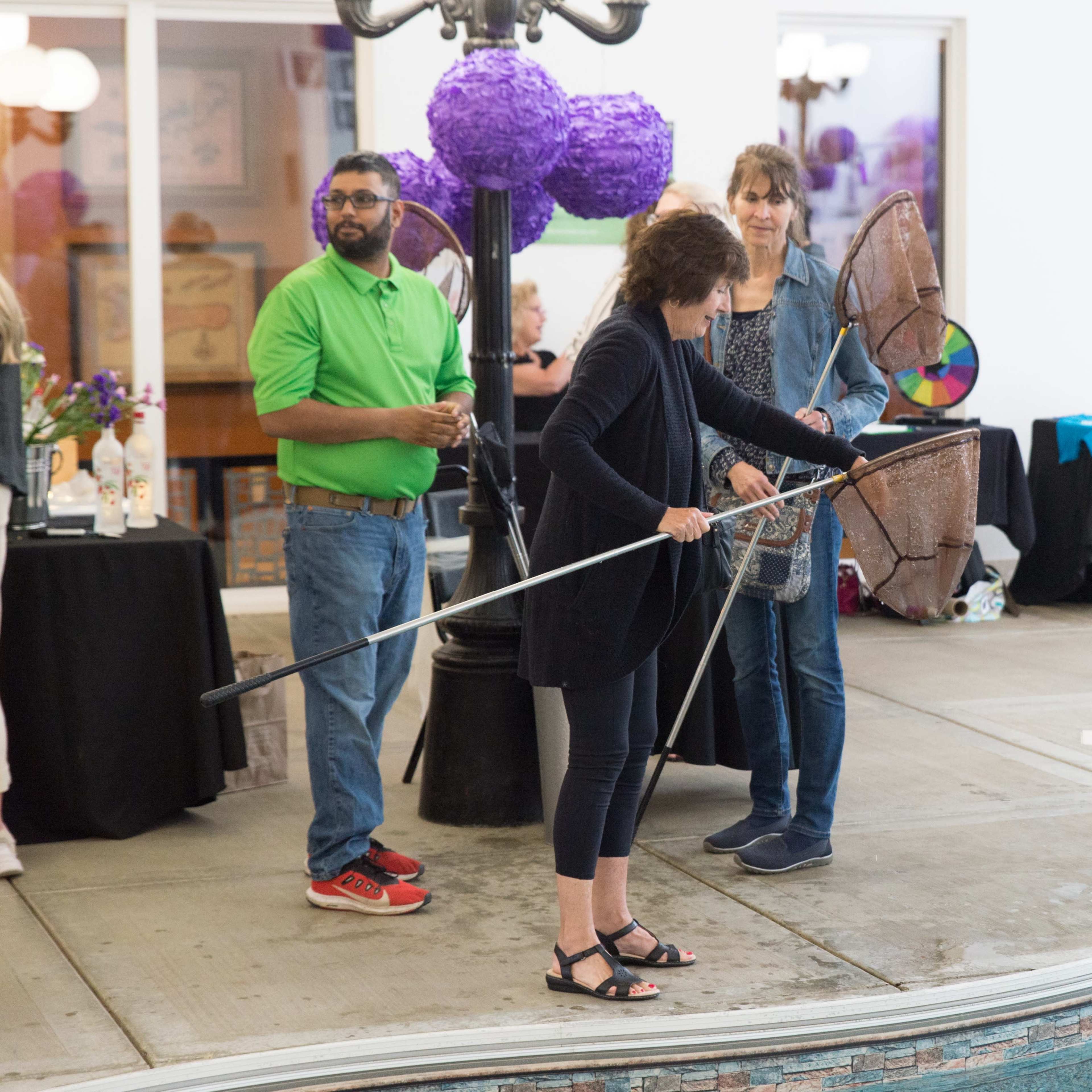 A woman uses a net to retrieve items from a pool while two other people observe.