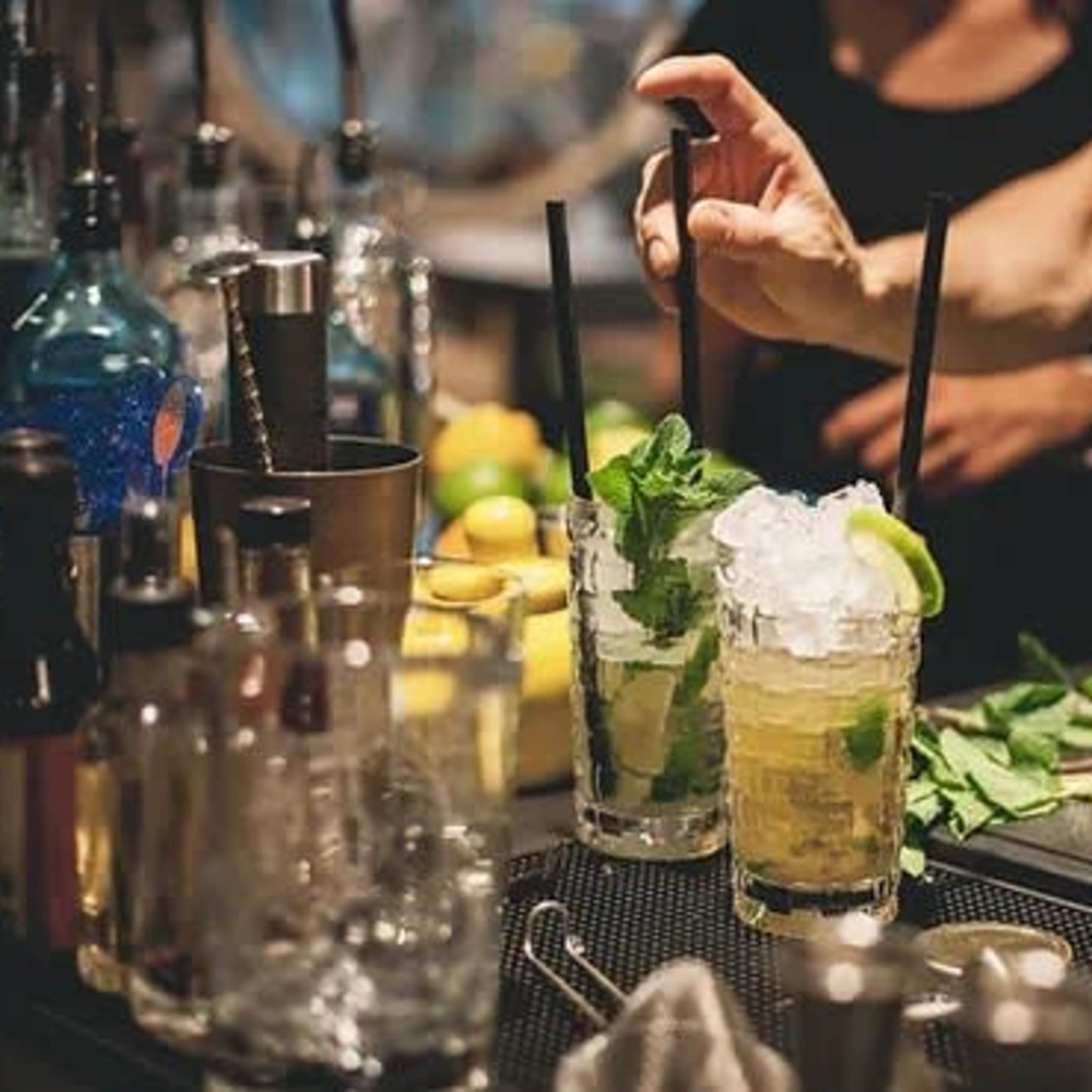 A bartender prepares cocktails with fresh mint and ice at a bar.