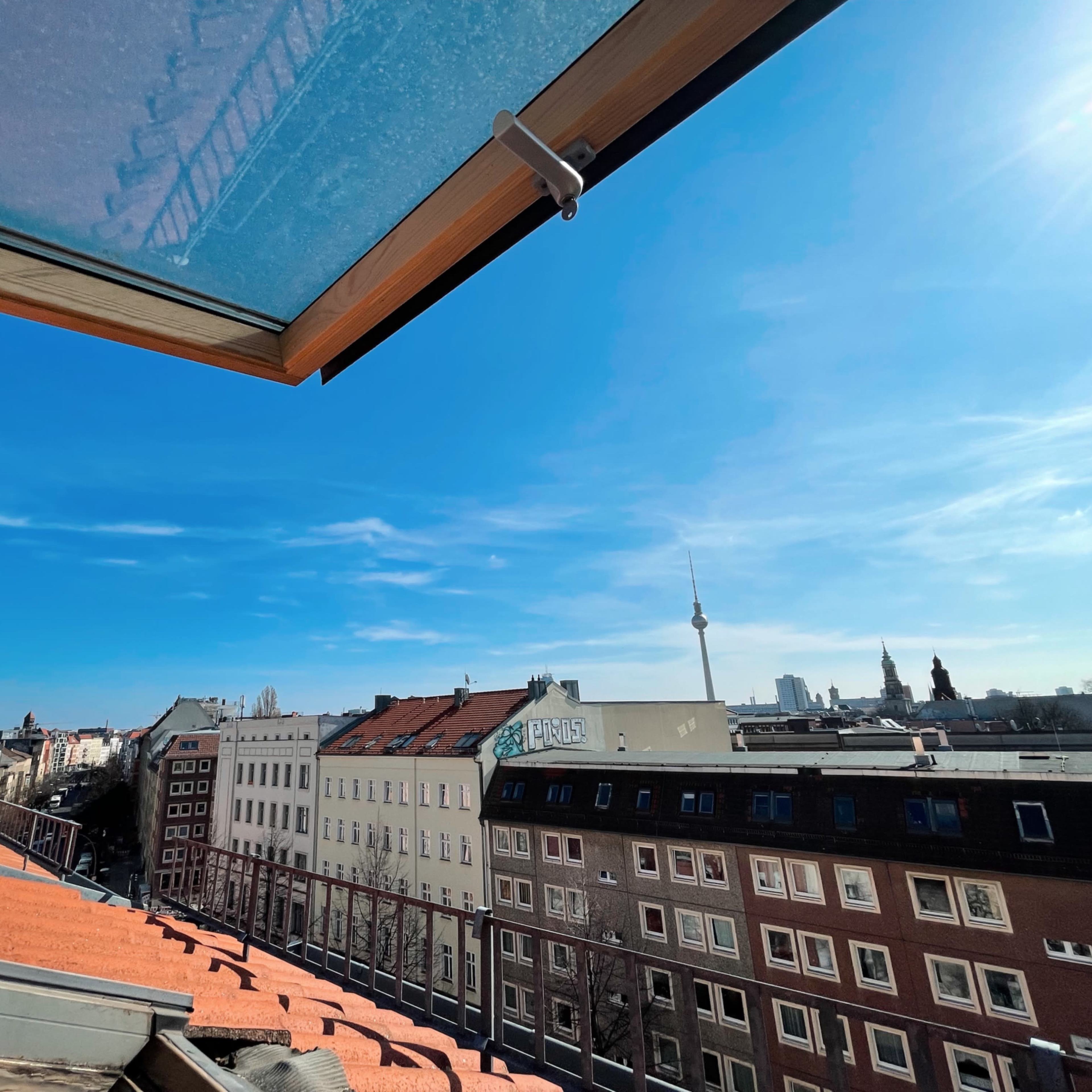 A view from a rooftop featuring red-tiled buildings and a clear blue sky, with a tower in the distance.