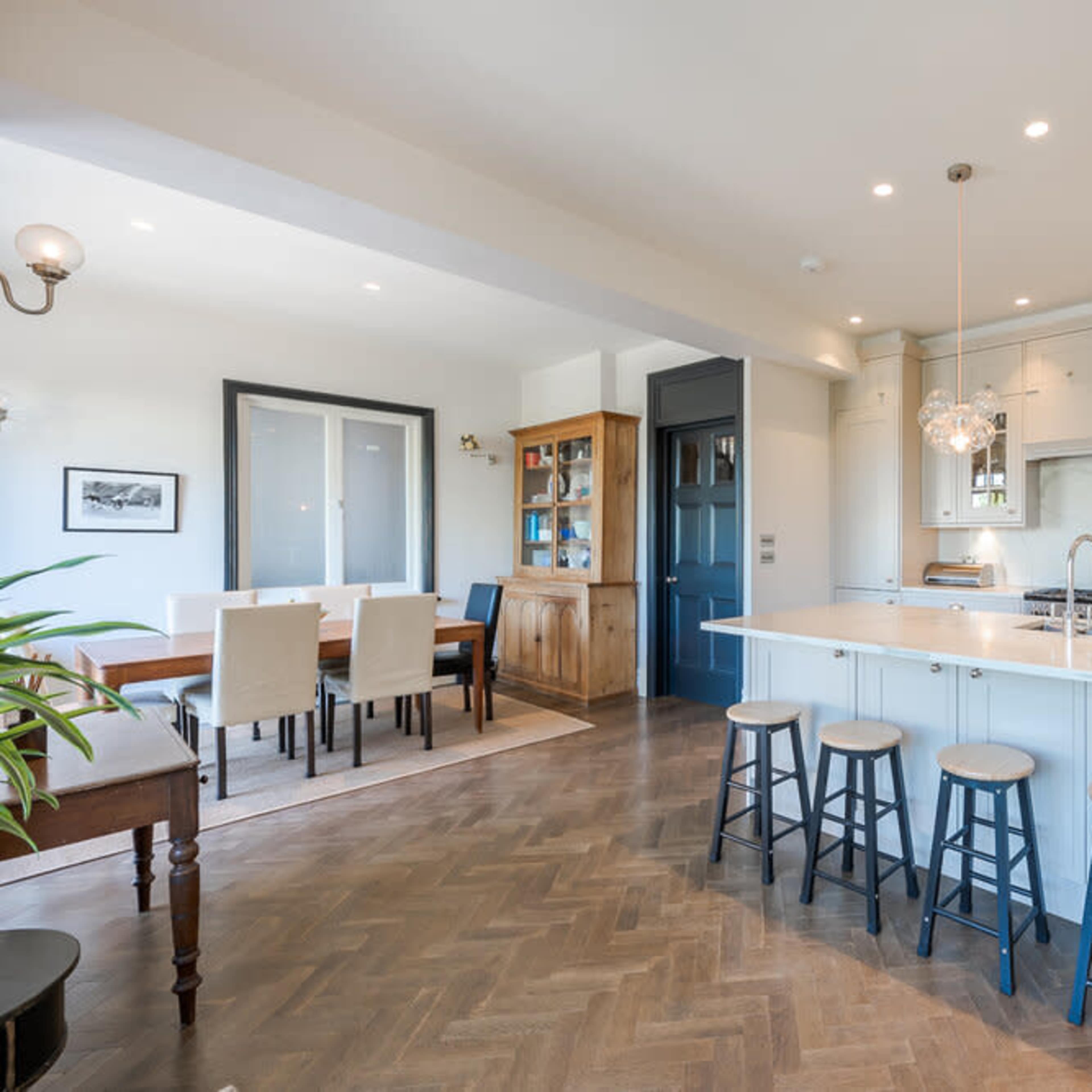 A modern kitchen features a large island with four stools, stainless steel appliances, and an adjacent dining area with a wooden table.