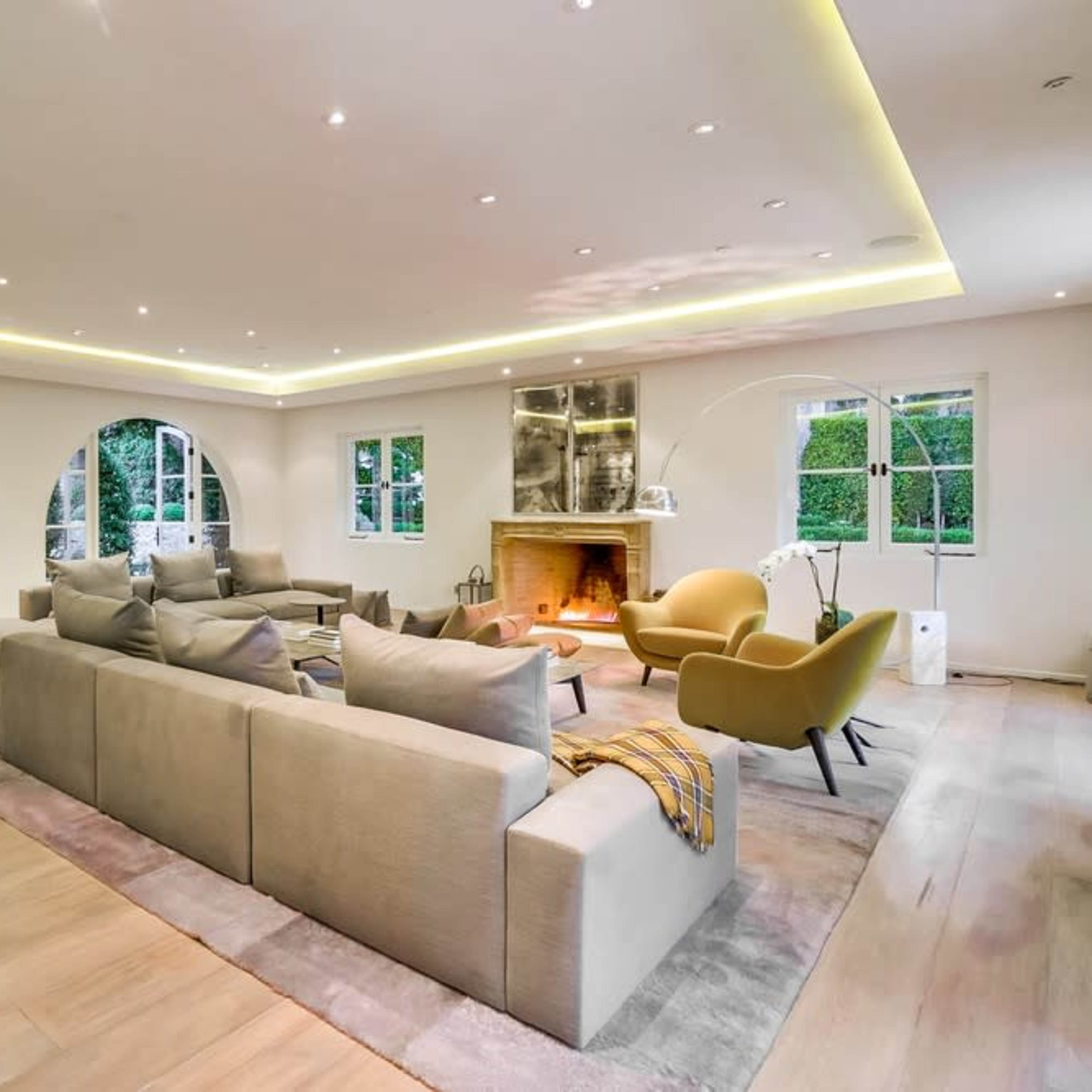 A spacious living room featuring a large sectional sofa, a fireplace, and a yellow armchair, illuminated by recessed lighting.