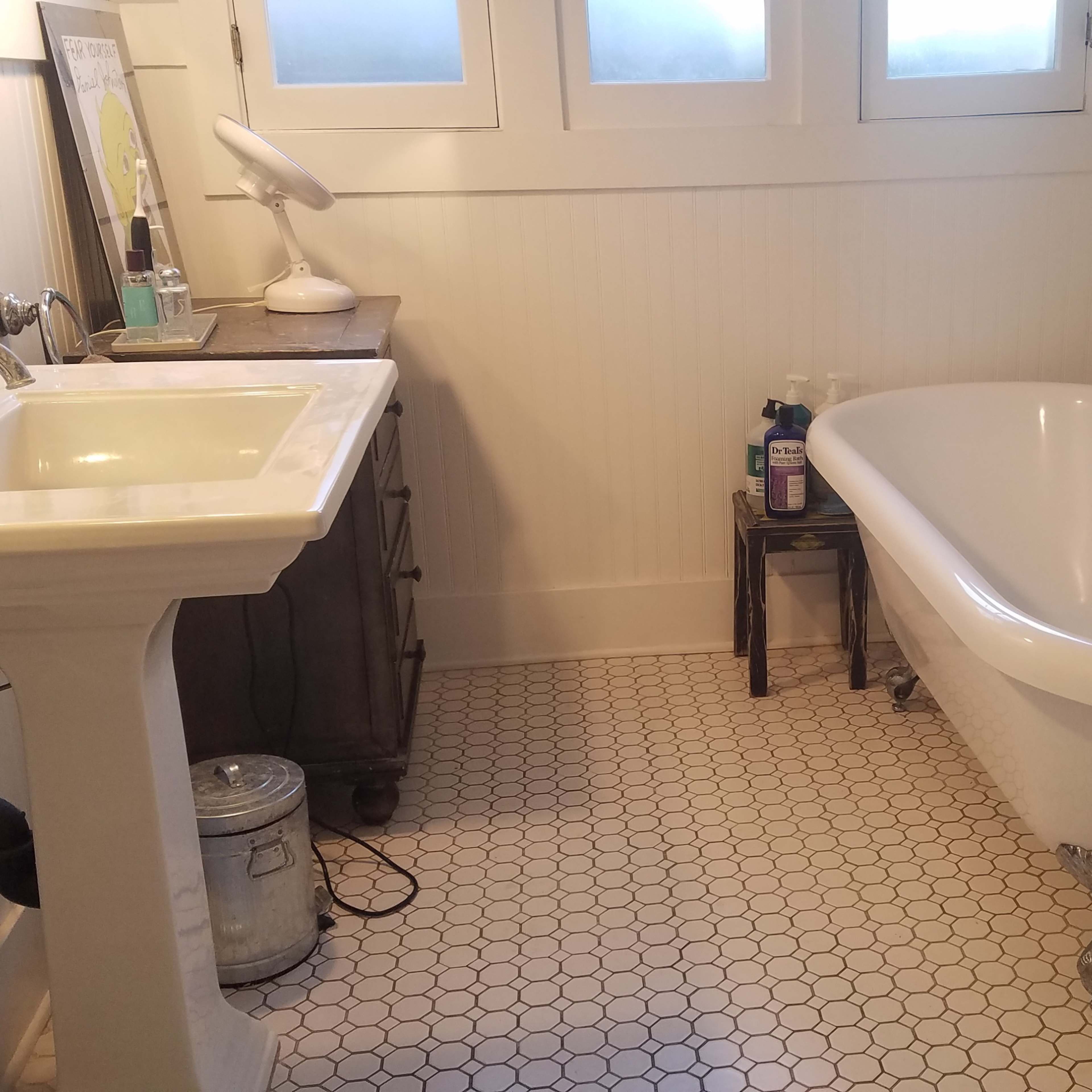 A clean bathroom featuring a freestanding bathtub, a pedestal sink, and a small side table with toiletries.