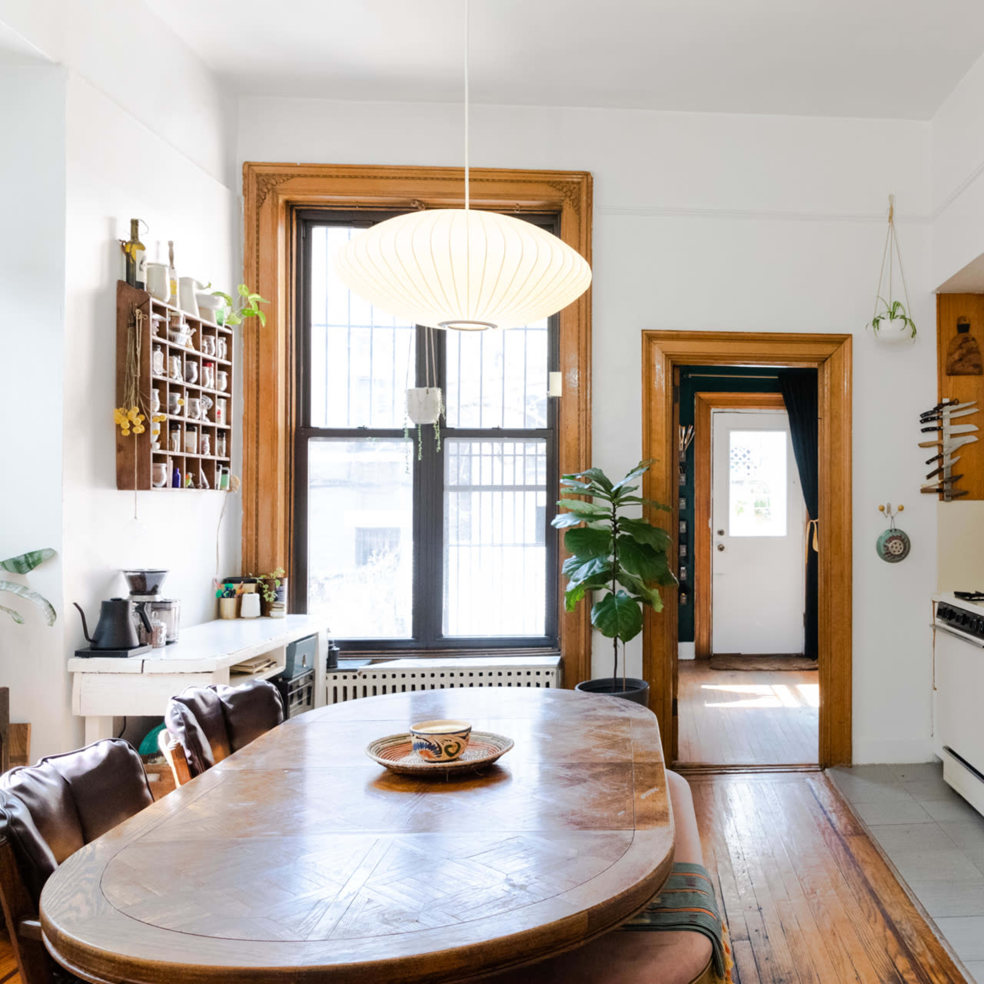 A well-lit kitchen features a wooden dining table, white cabinets, and a doorway leading to an outdoor space.