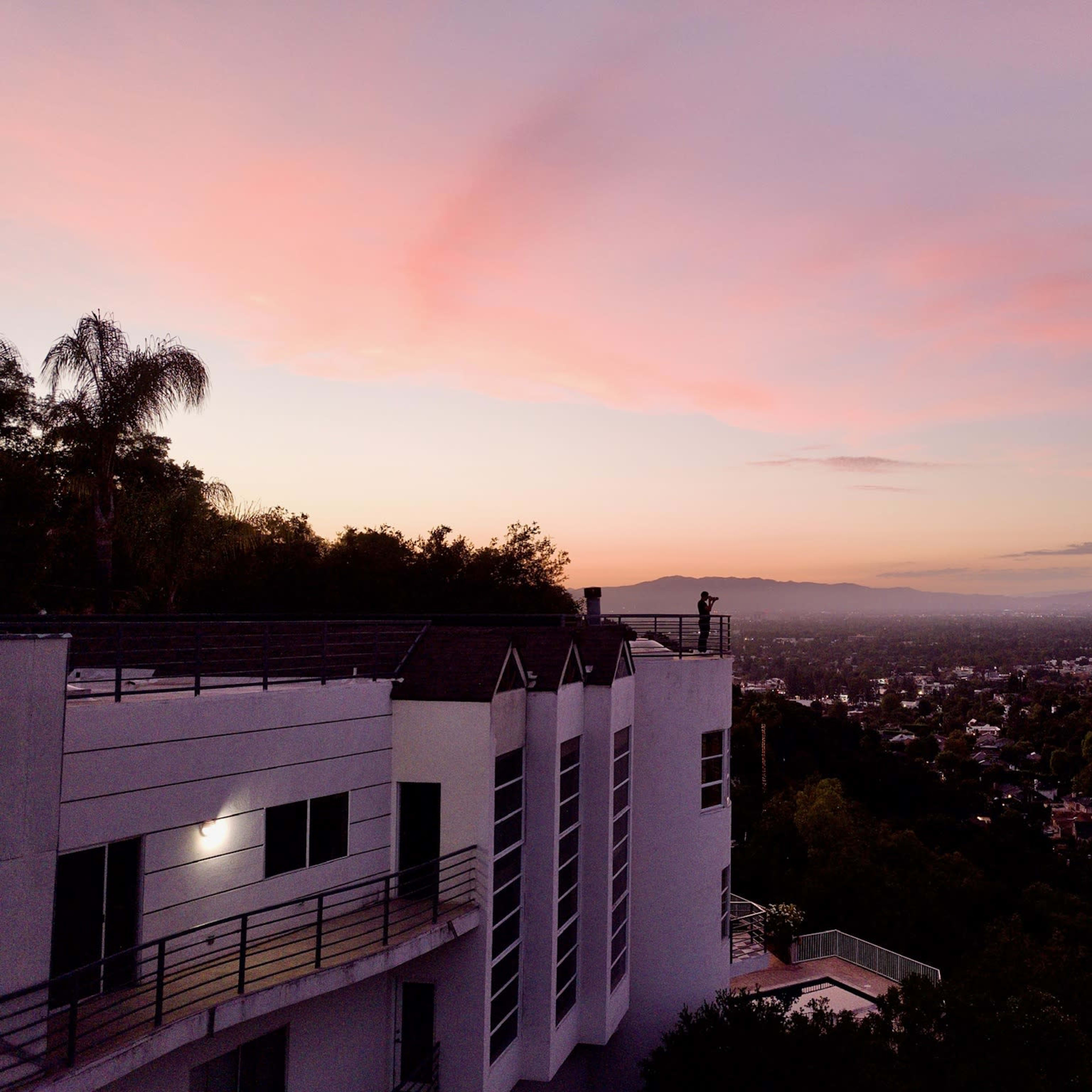 A hillside building overlooks a valley with a sunset-lit sky in the background.