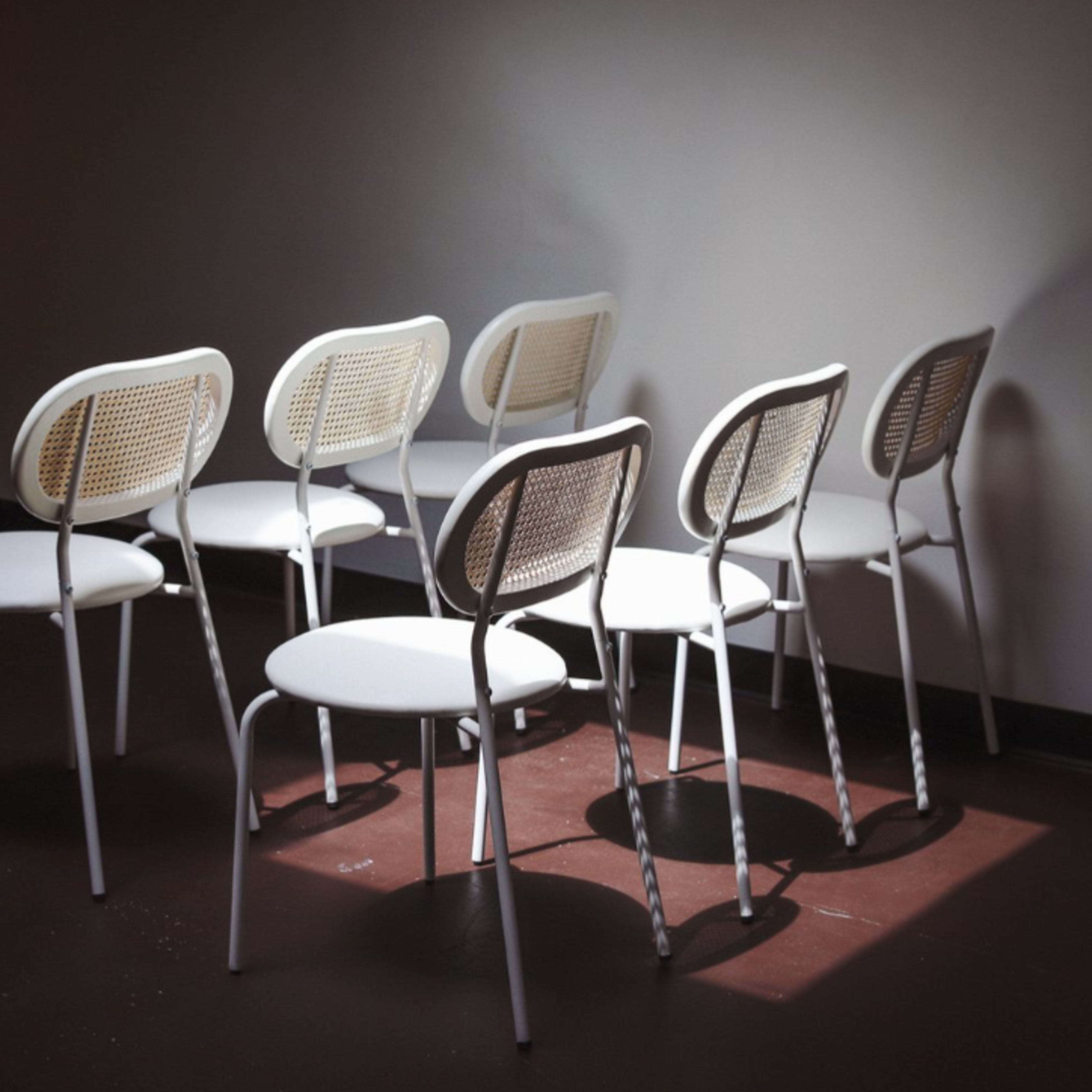 A row of white chairs with woven backs is arranged in a dimly lit room.