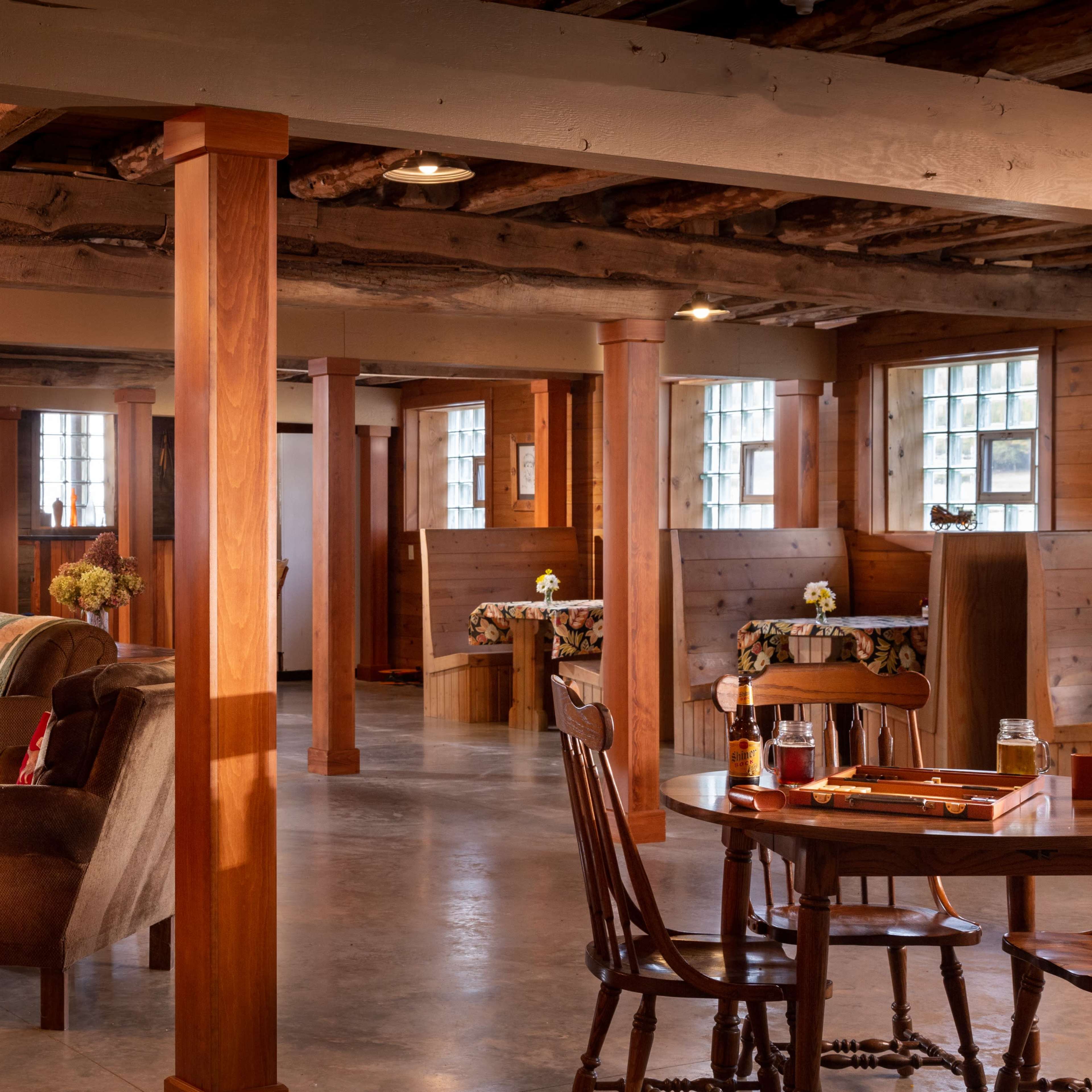A spacious, wooden-paneled room with several seating areas, light wooden columns, and tables adorned with tablecloths.