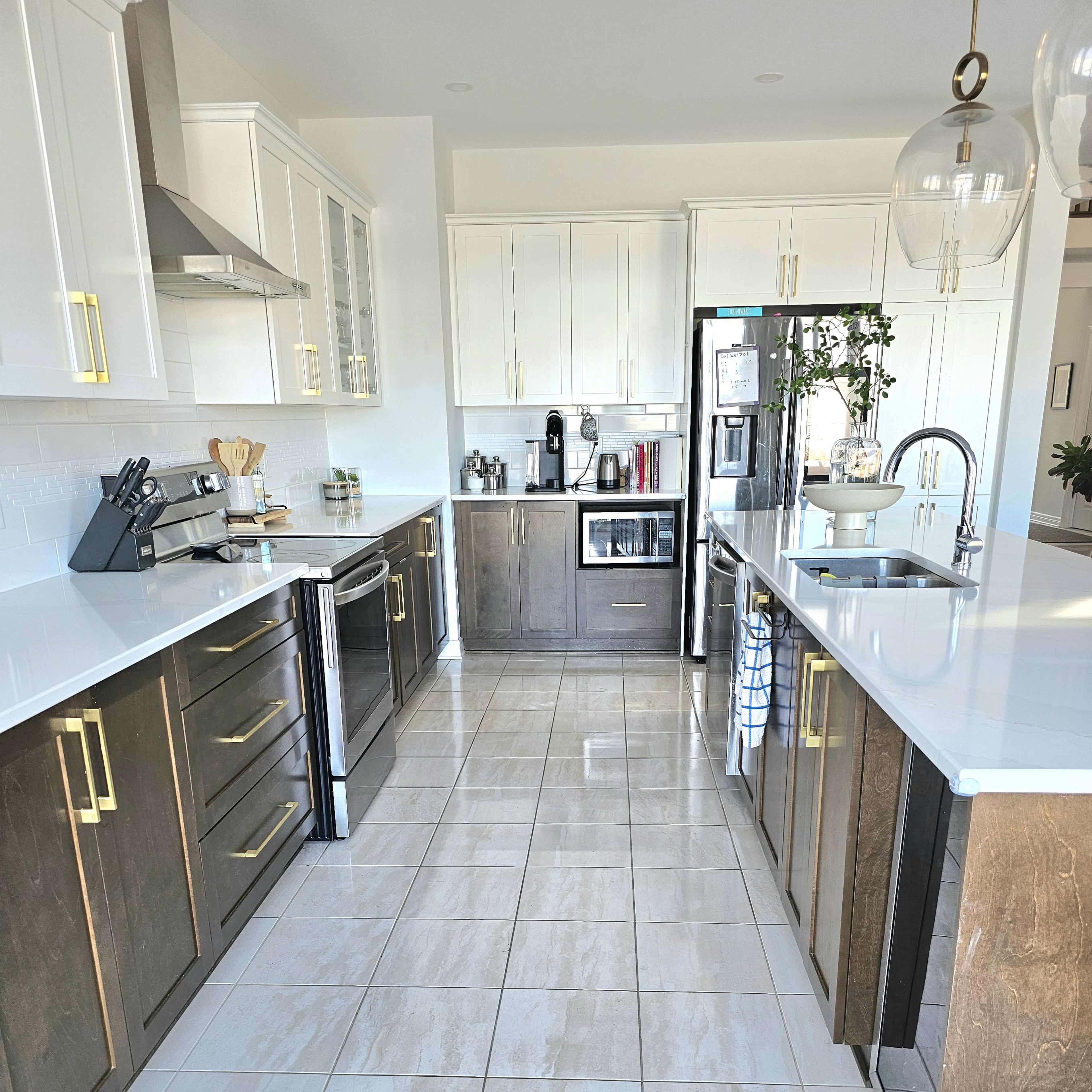 A modern kitchen features white cabinets with gold handles, a central island, stainless steel appliances, and tiled flooring.