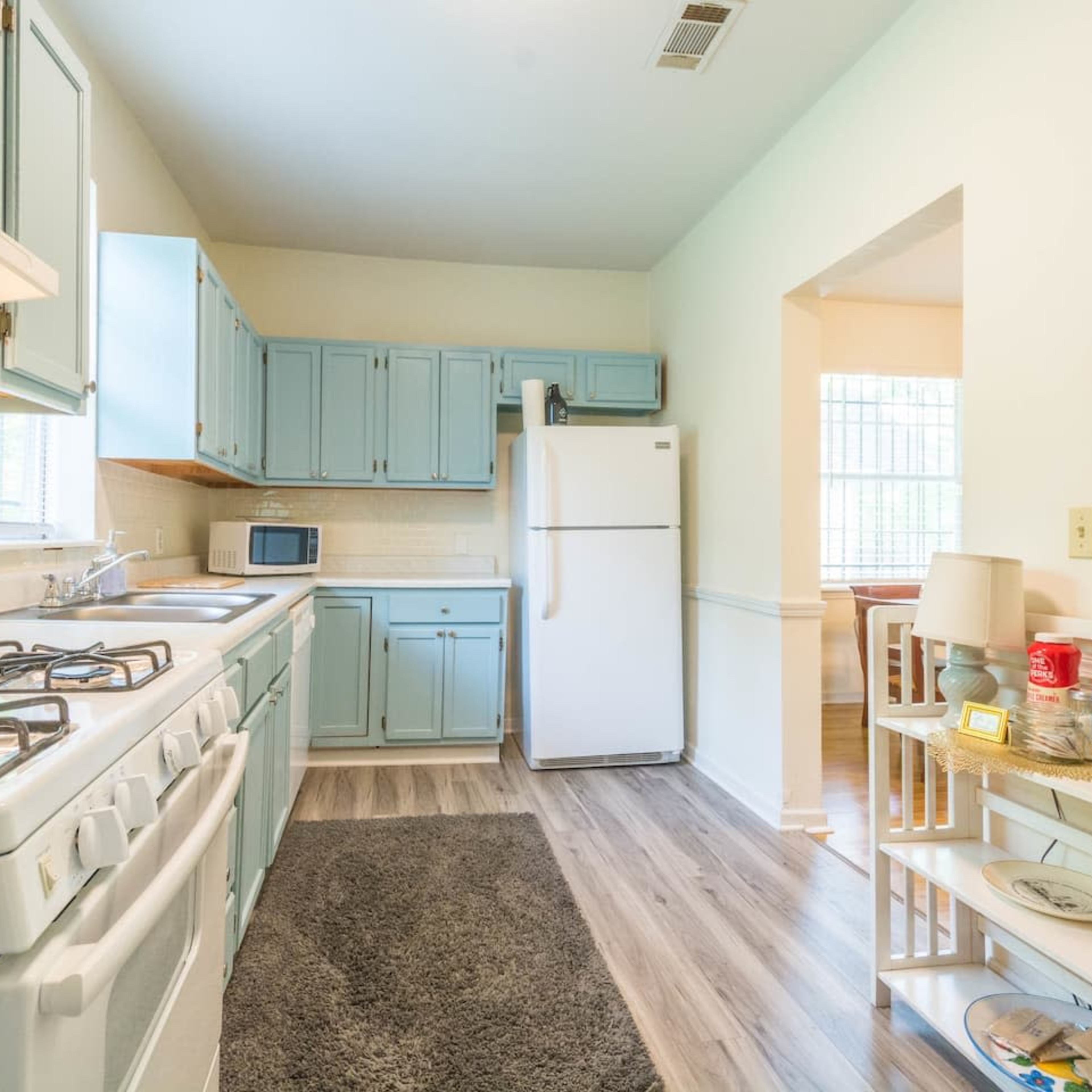 The kitchen features light blue cabinetry, a white stove and refrigerator, and a small table with items on it.