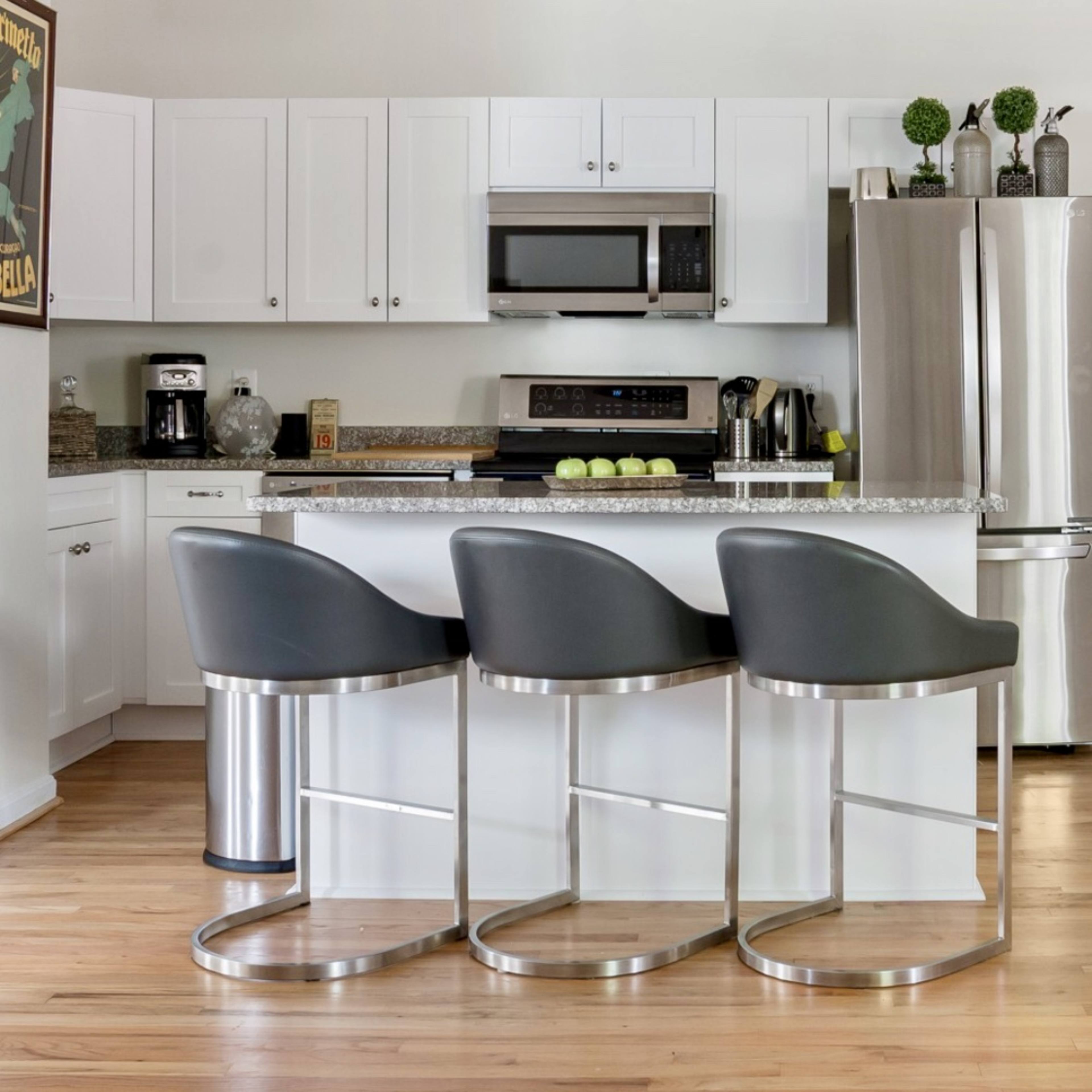 A modern kitchen features white cabinetry, stainless steel appliances, and three gray bar stools at a central island.