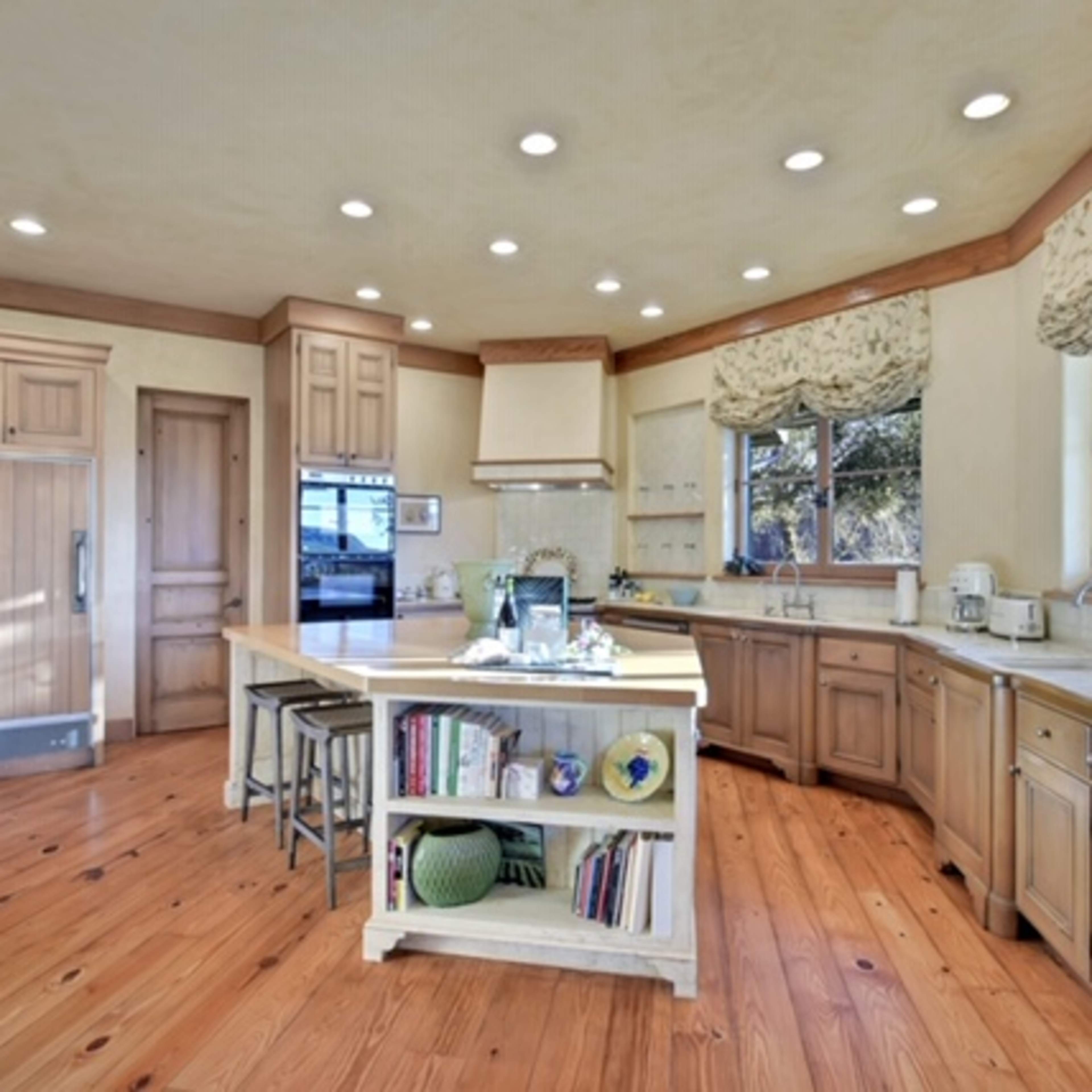 A spacious kitchen with wooden cabinetry, a central island, and large windows allowing natural light to enter.