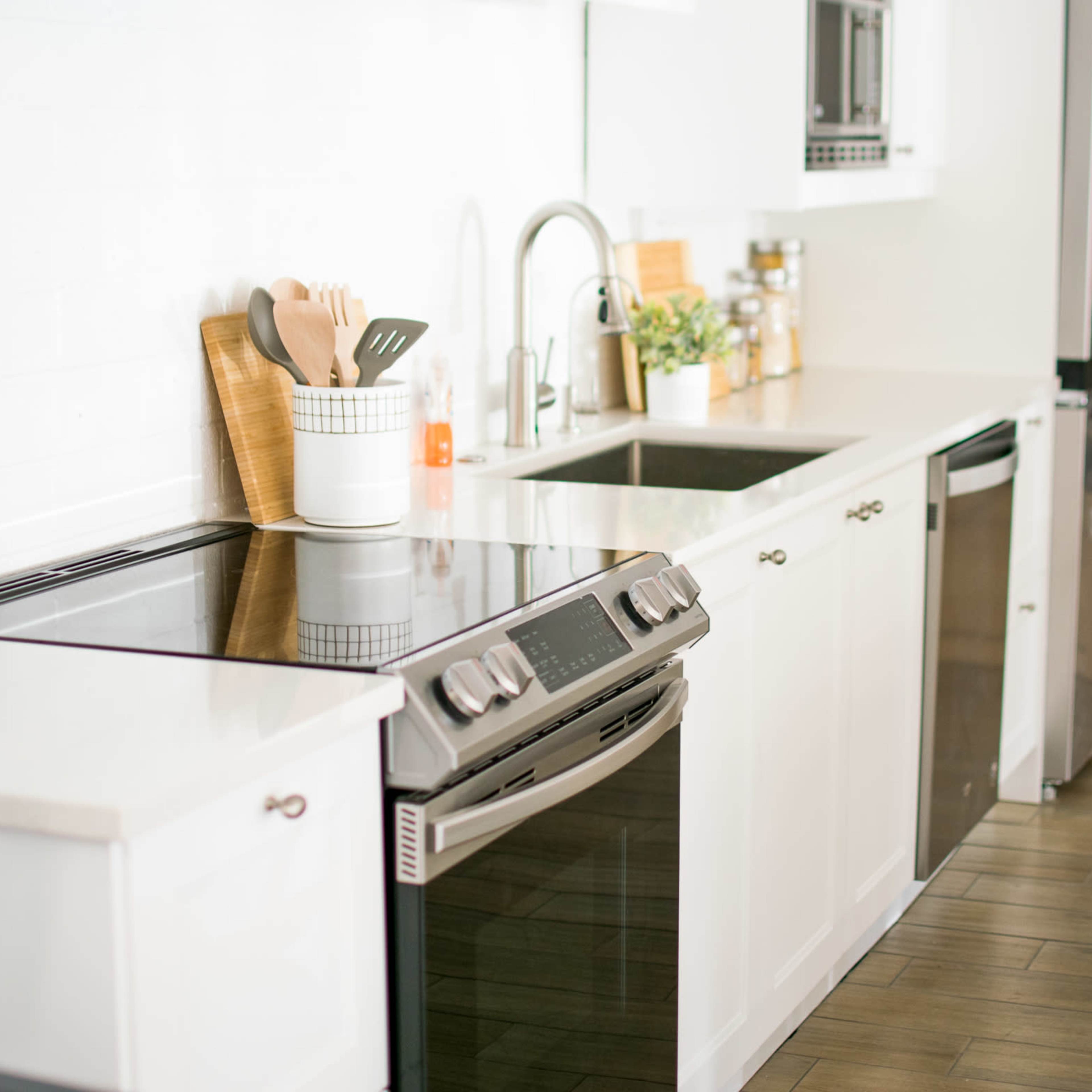 A modern kitchen with a sleek countertop, a stainless steel stove, and organized utensils in a container next to a sink.
