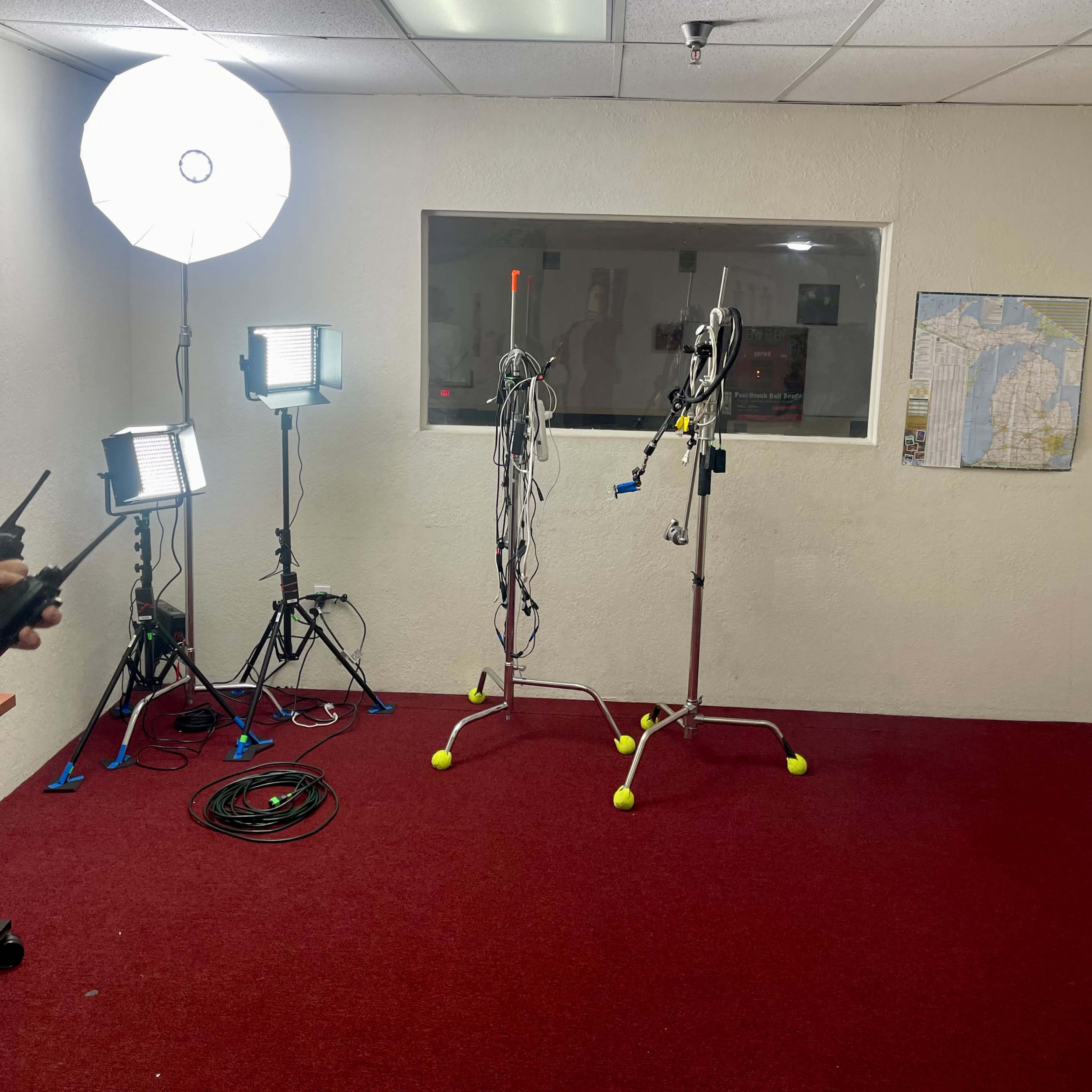 A room with red carpet, two metal stands with cables, and multiple lighting setups on the left.