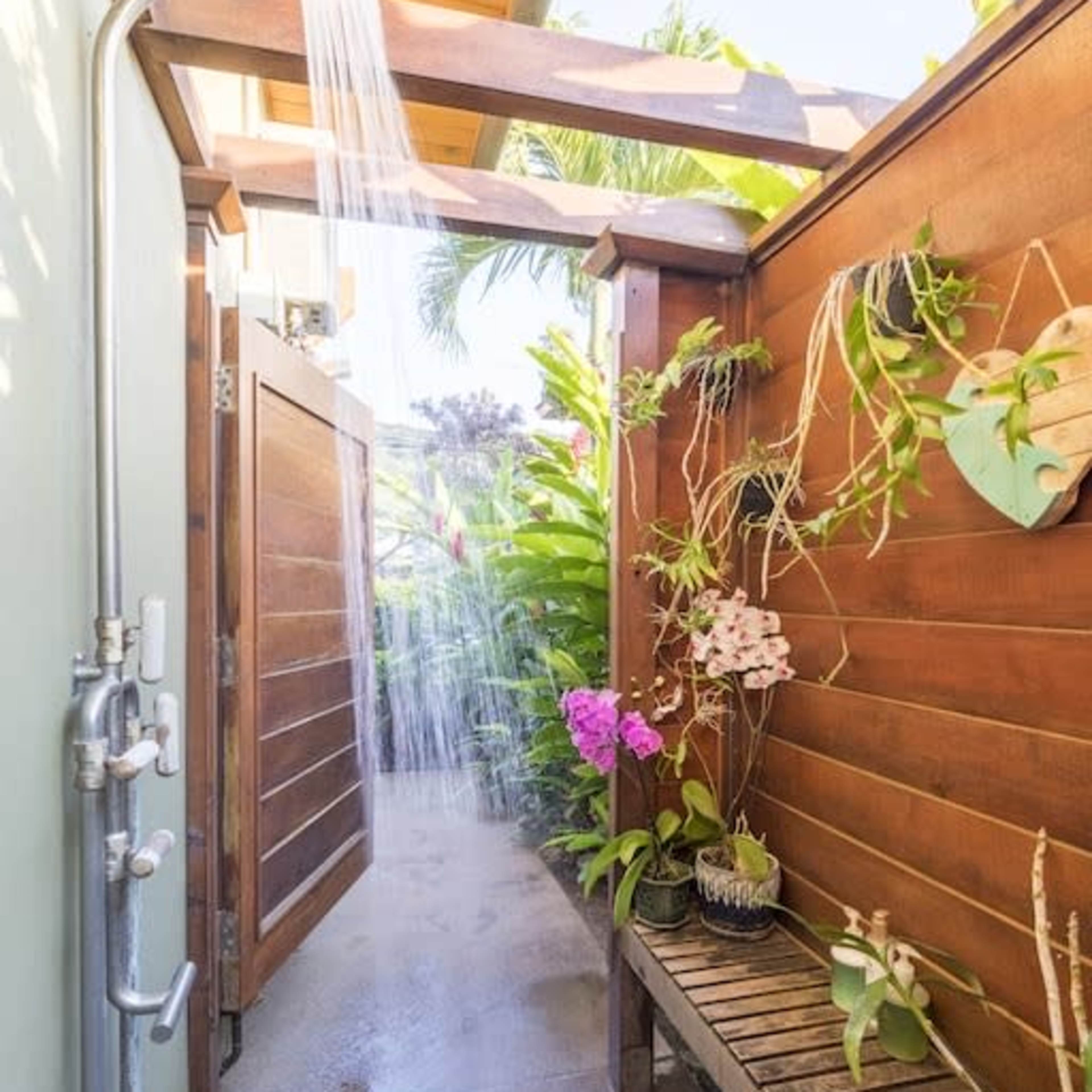 An outdoor shower area features a wooden surround with potted plants and a bench along one side.