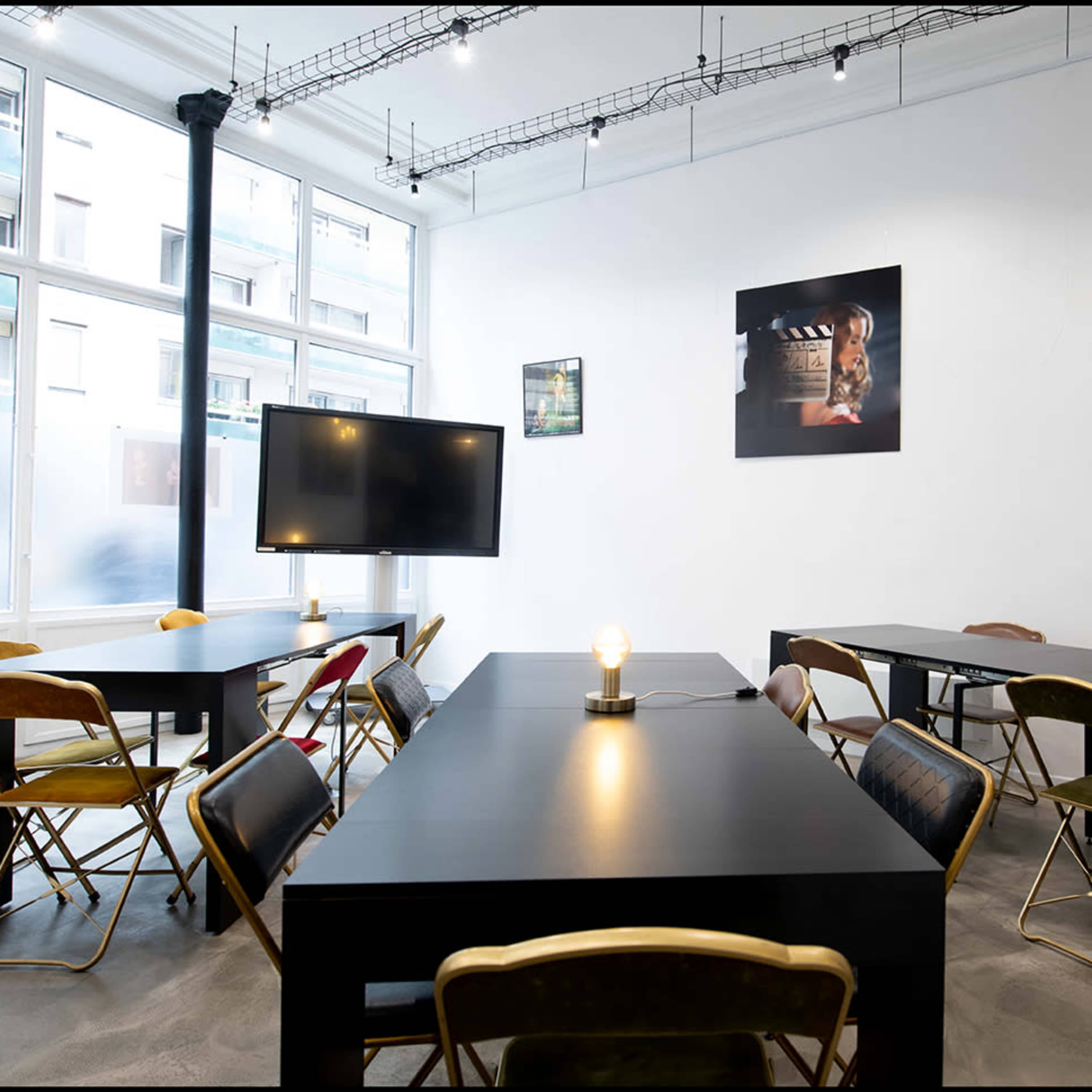 A modern meeting room with several black tables and multi-colored chairs arranged around the space.