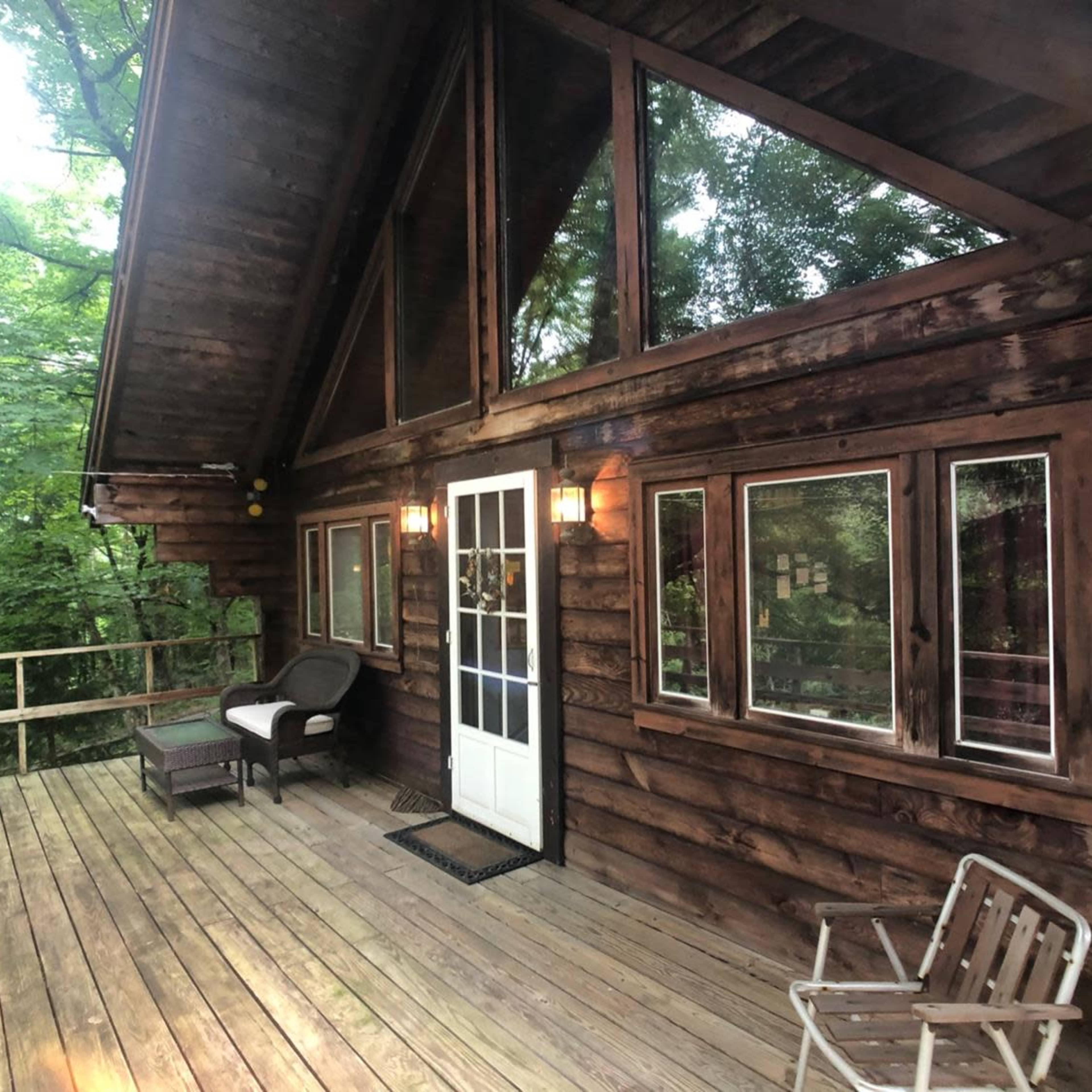 A rustic wooden cabin with large windows and a porch overlooking a forested area.