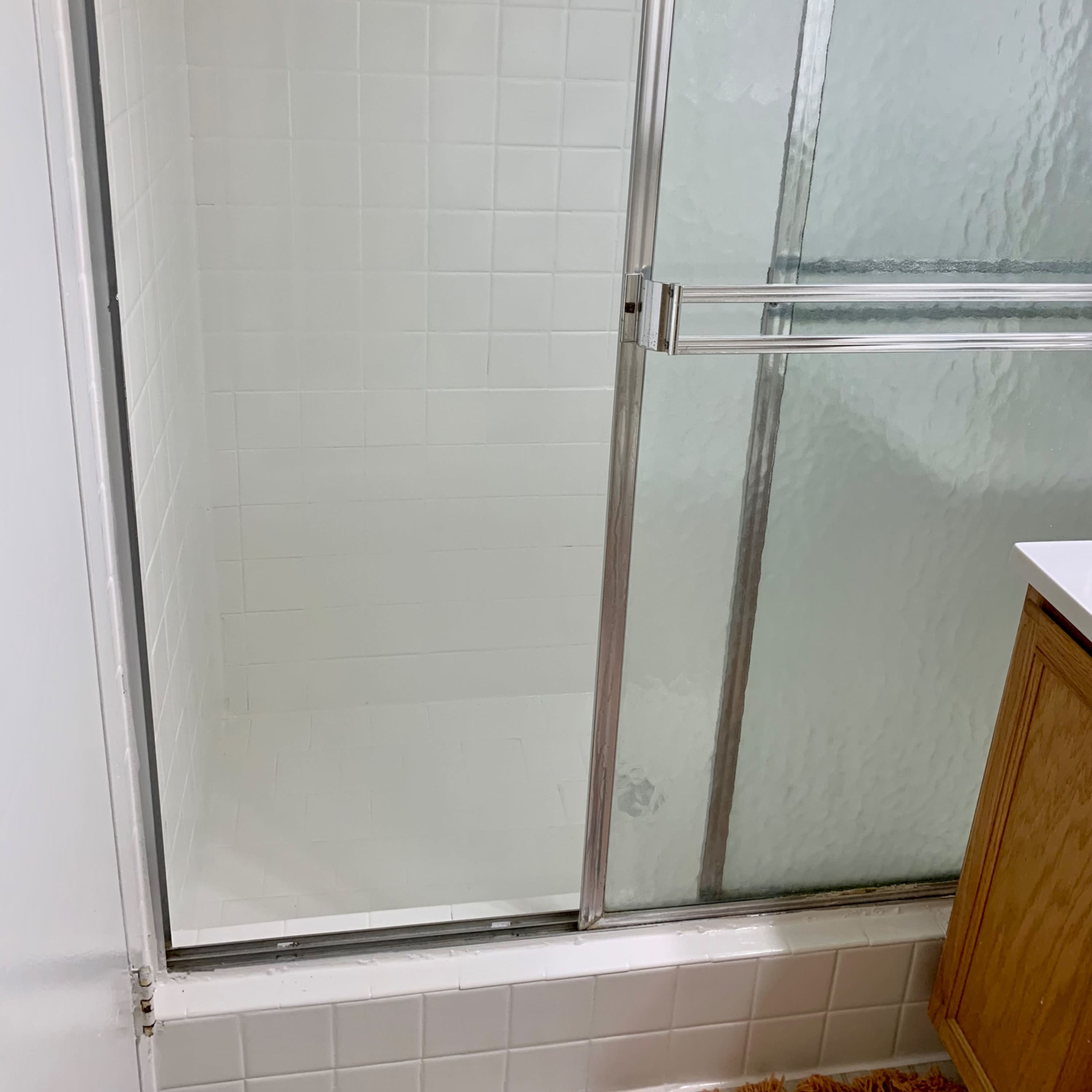 A shower stall with clear glass doors and tiled walls, featuring a small vanity unit nearby.