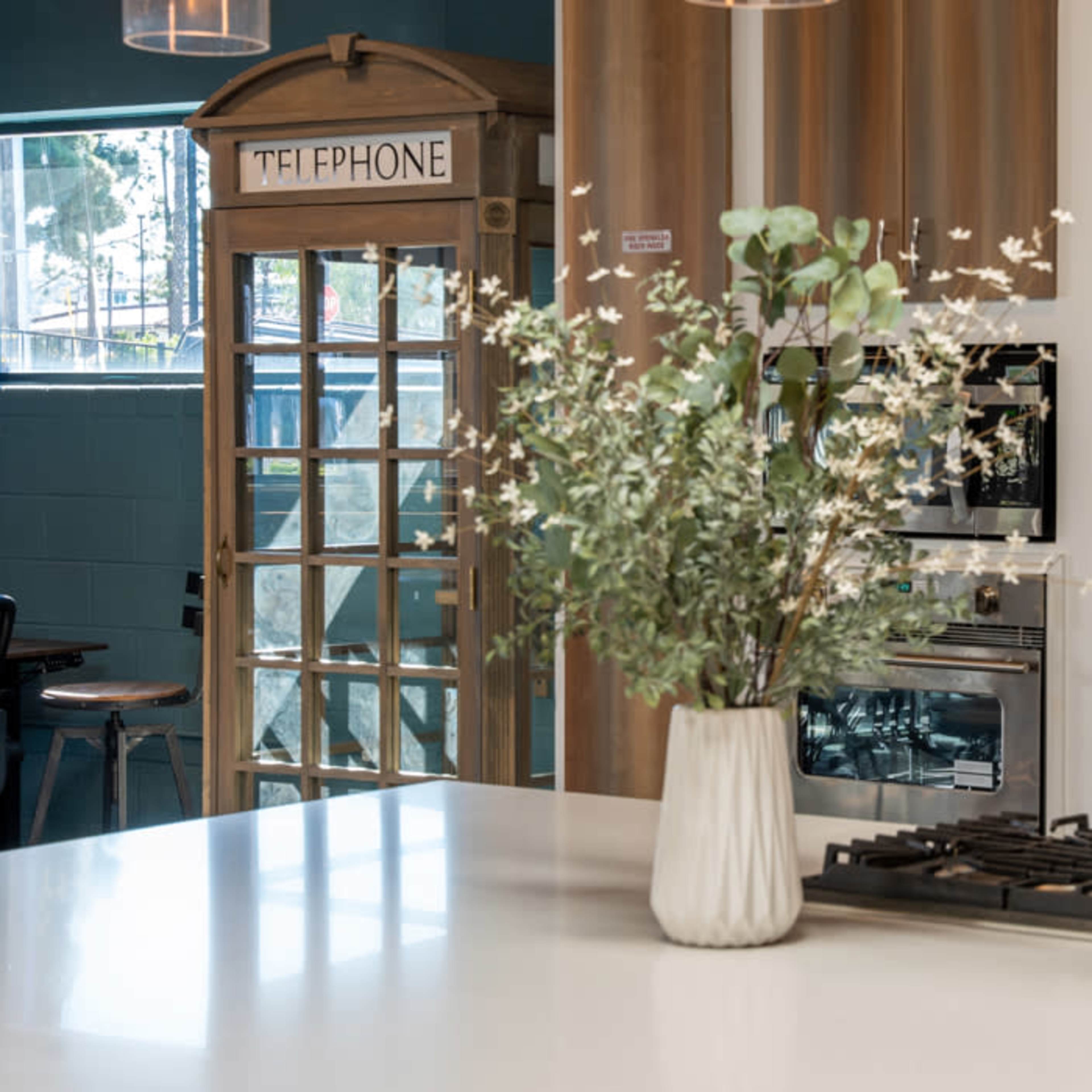 A modern kitchen features a gas stove, a vase of flowers, and a vintage telephone booth in the background.