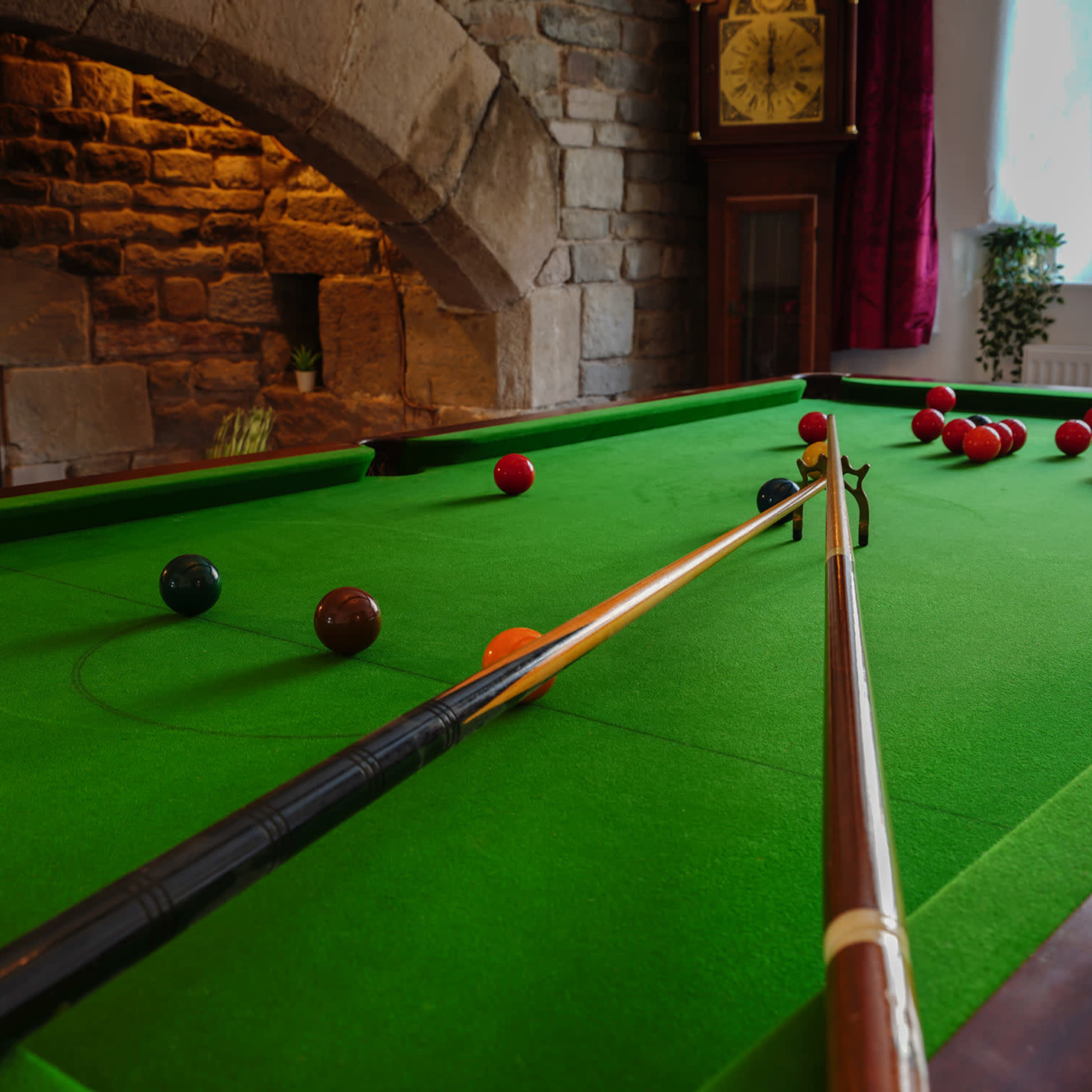 A well-lit billiard table with several colorful balls arranged on green felt, alongside two cues resting on the table.