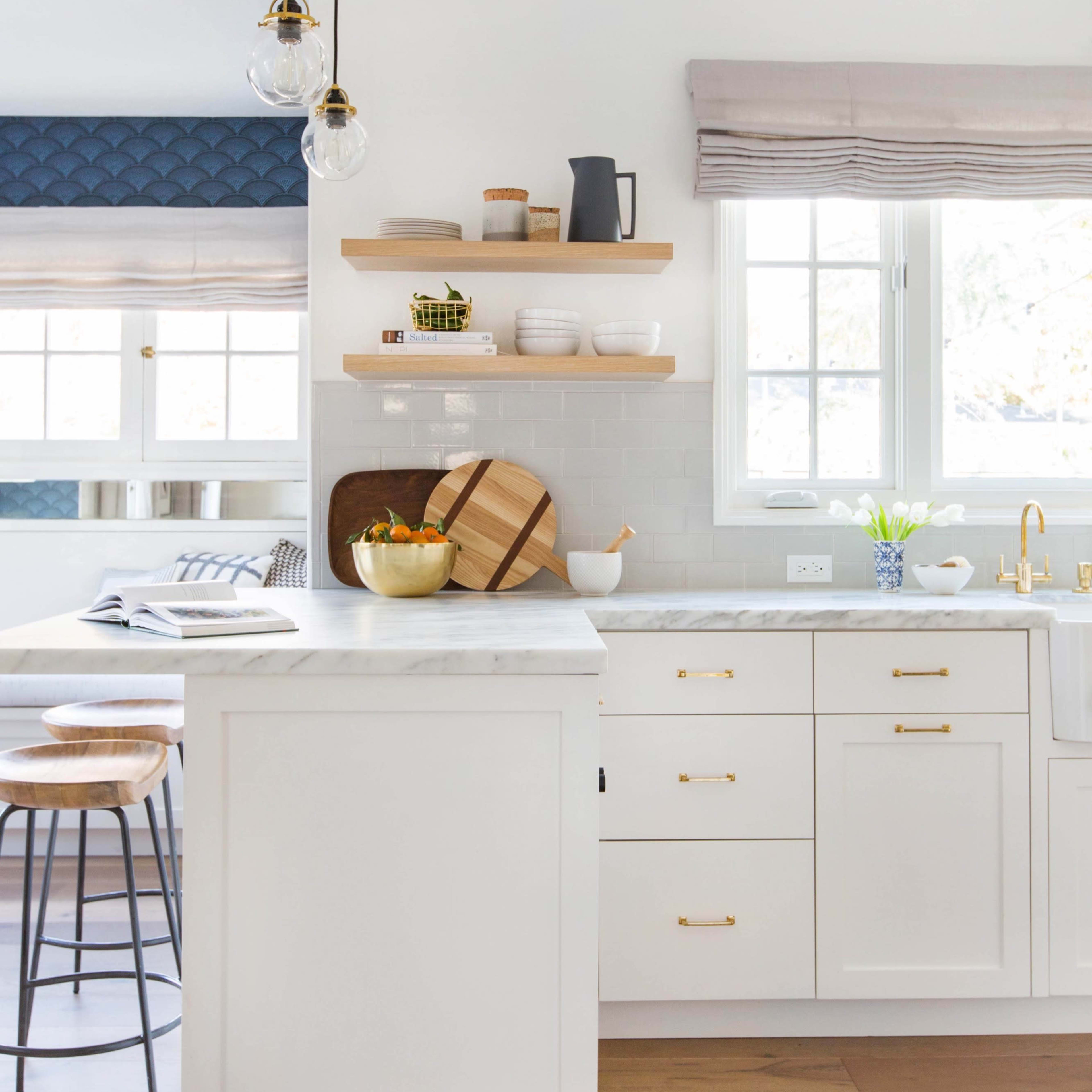 A modern kitchen with white cabinetry, open shelves displaying dishes, and a large island with bar stools.