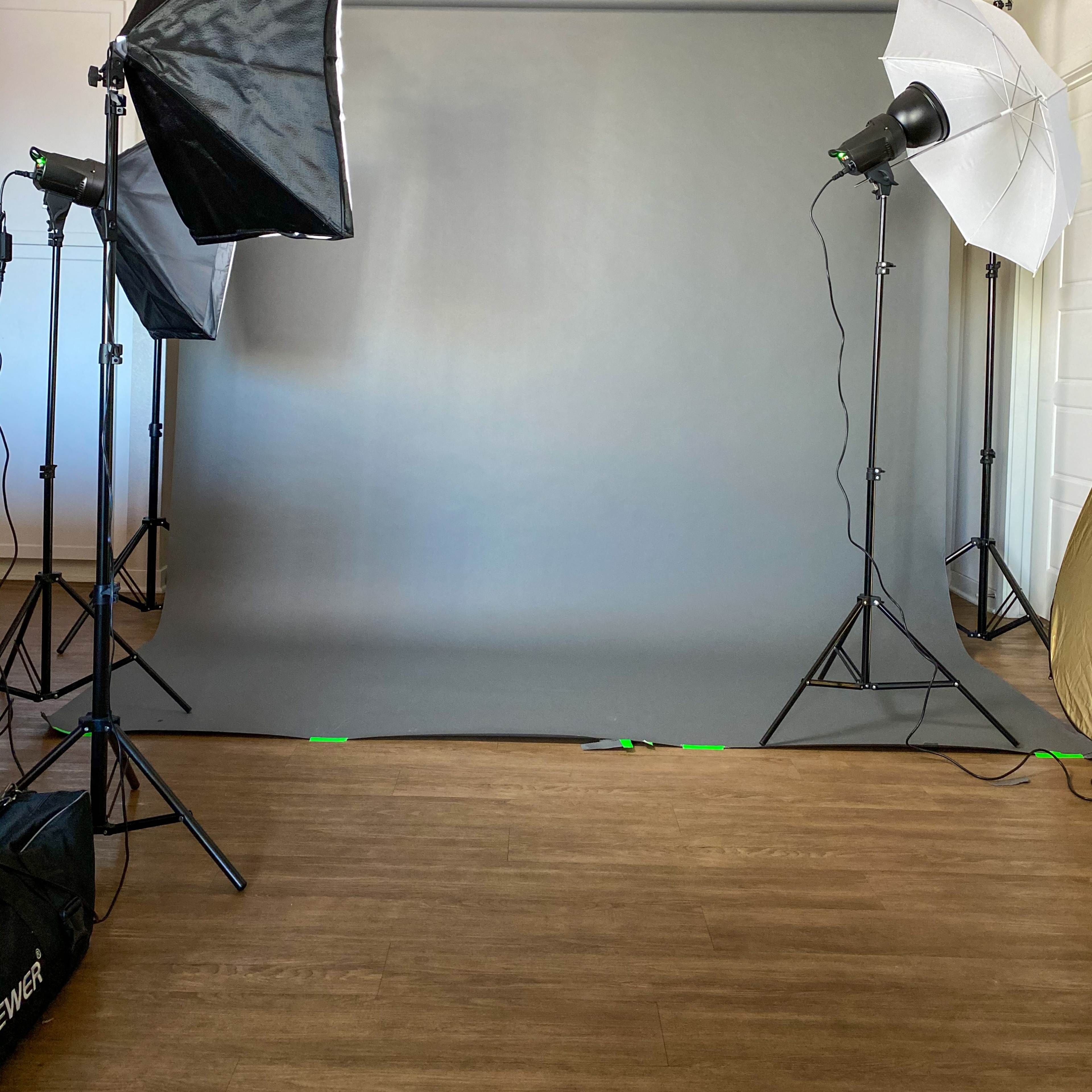 A photography studio setup with a gray backdrop and lighting equipment on either side.